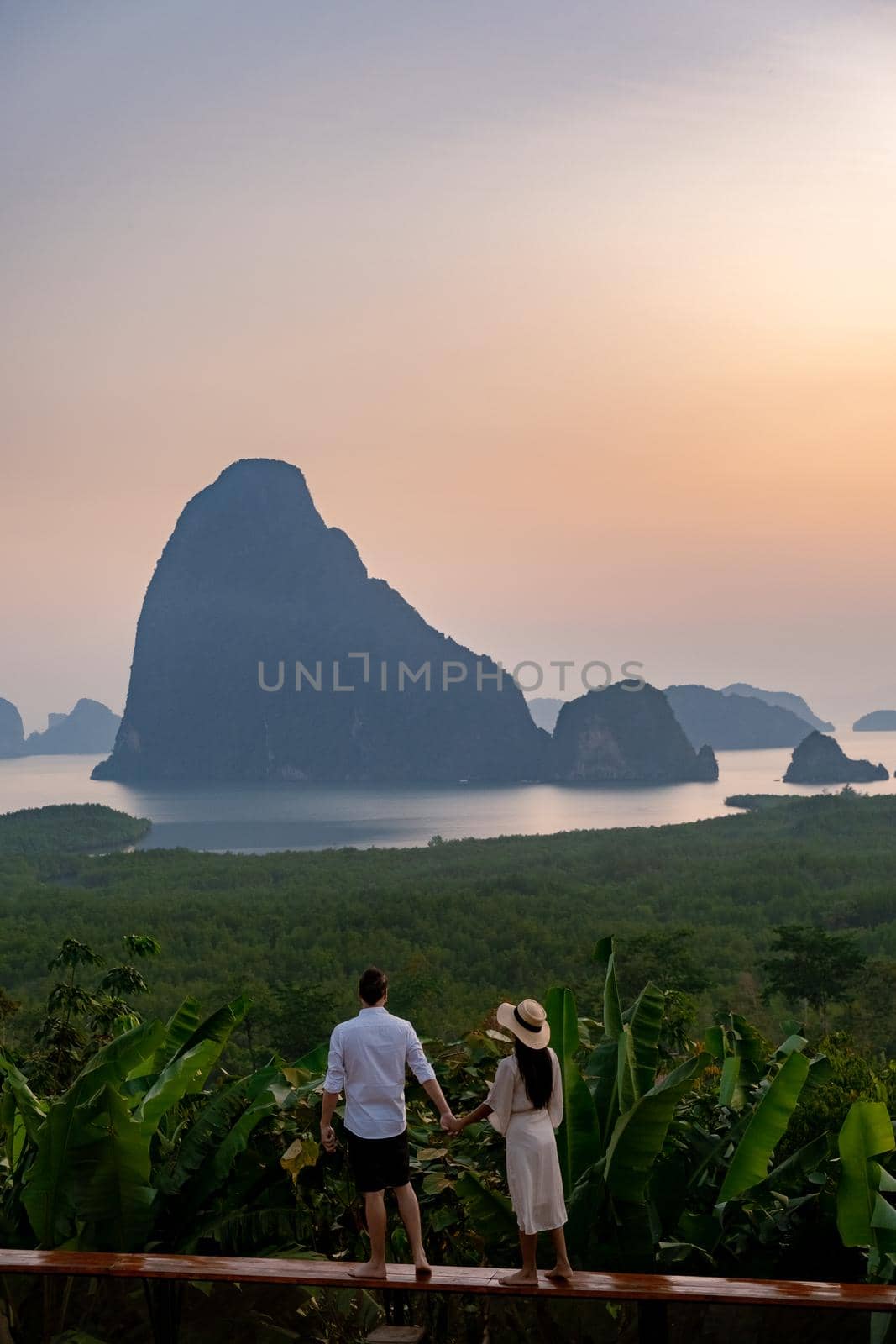 couple men and woman mid age watching sunrise in Phangnga bay Thailand, Phangan bay viewpoint, couple watching sunrise on the edge of a swimming pool, infinity pool look out over Phangnga Bay Thailand