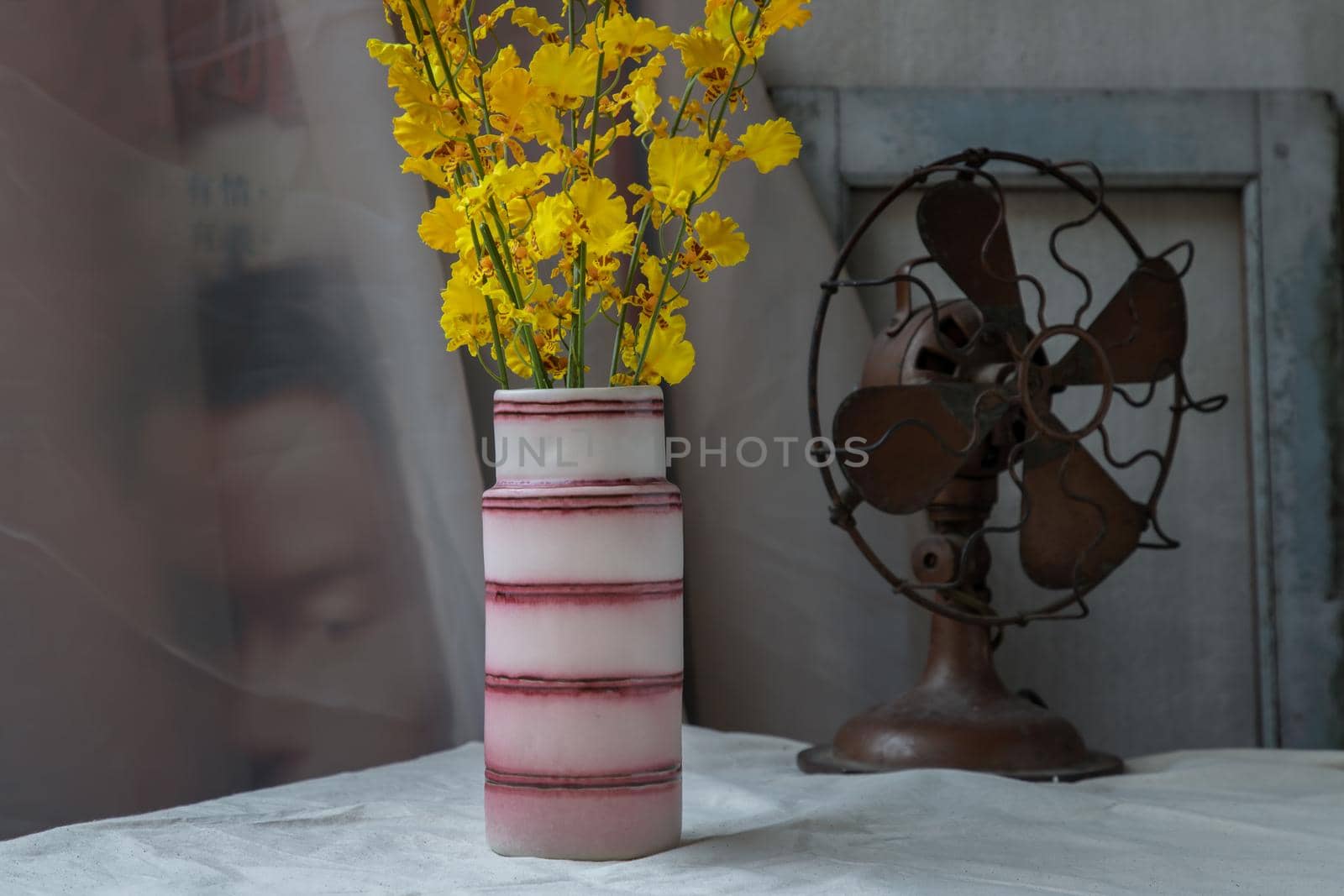 Bouquet of yellow flowers in Pink handmade ceramic vase and Vintage fan on white textured table cloth with old cement wall. Home decor, Selective focus.