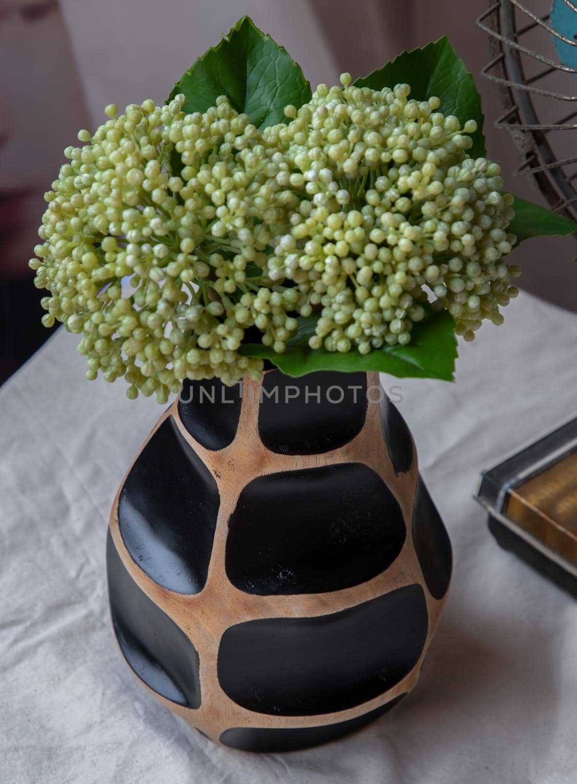 Bouquet of green in Handmade wooden vase and Vintage fan on white textured table cloth with old cement wall. Home decor, Selective focus.