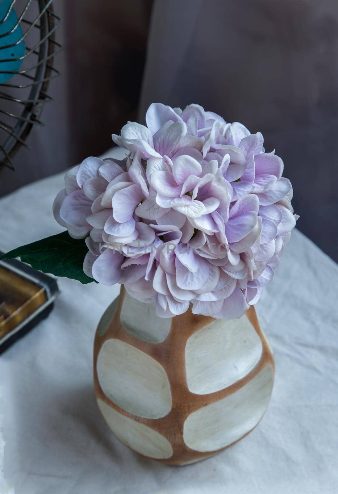 Bouquet of purple in Handmade wooden vase and Vintage fan on white textured table cloth with old cement wall. Home decor, Selective focus.