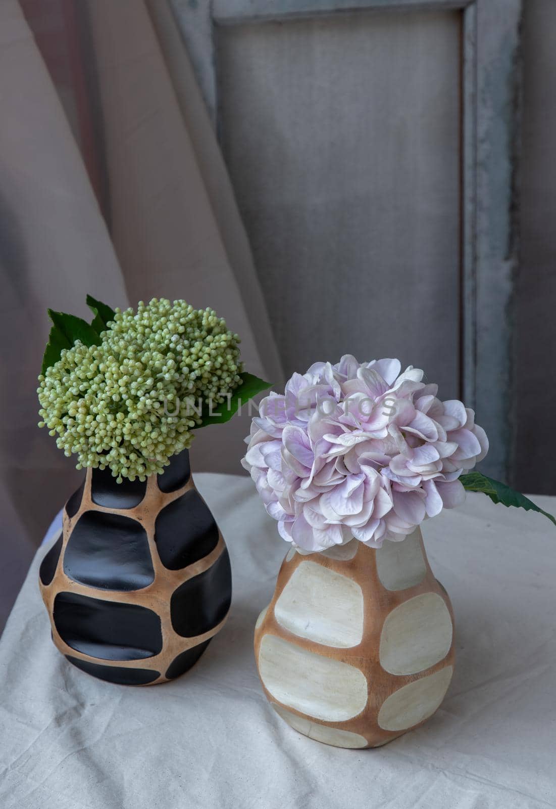 Bouquet of green and purple in Two handmade wooden vase on white textured table cloth with old cement wall. Home decor, Selective focus.