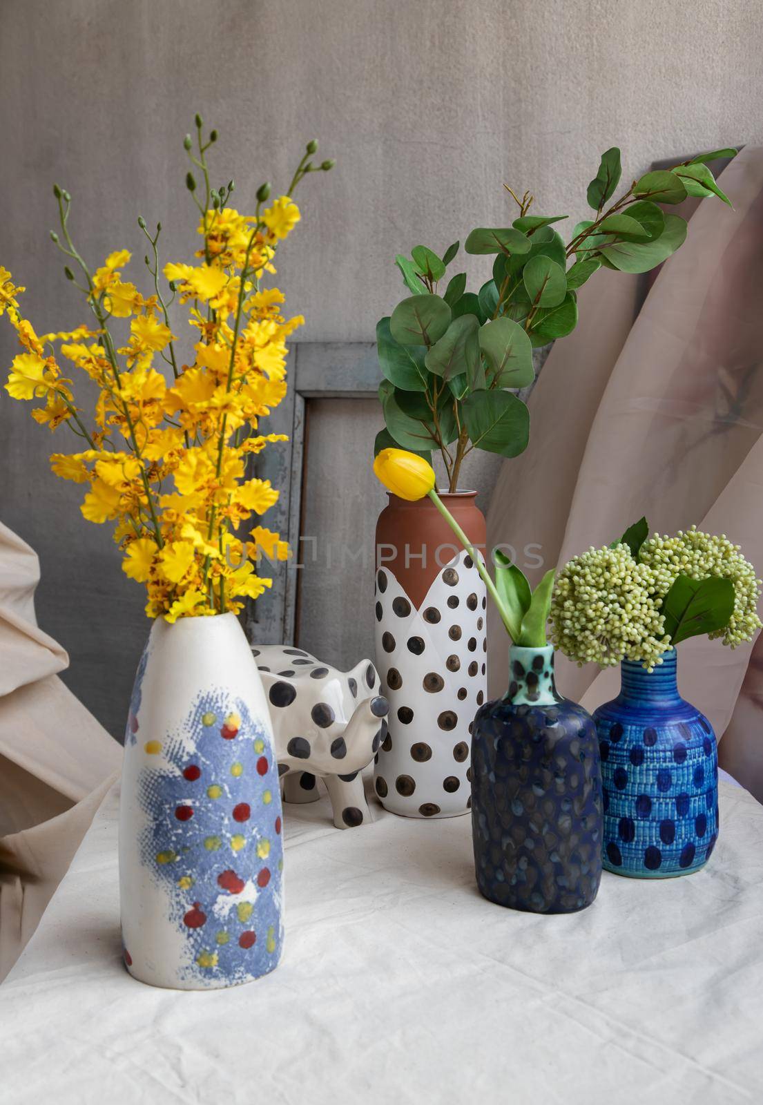 Bouquet of many flowers in Handmade Assorted Many Different Ceramic Polka Dotted Vases and Elephant shaped ceramic on white textured table cloth. Home decor, Space for text, Selective focus.