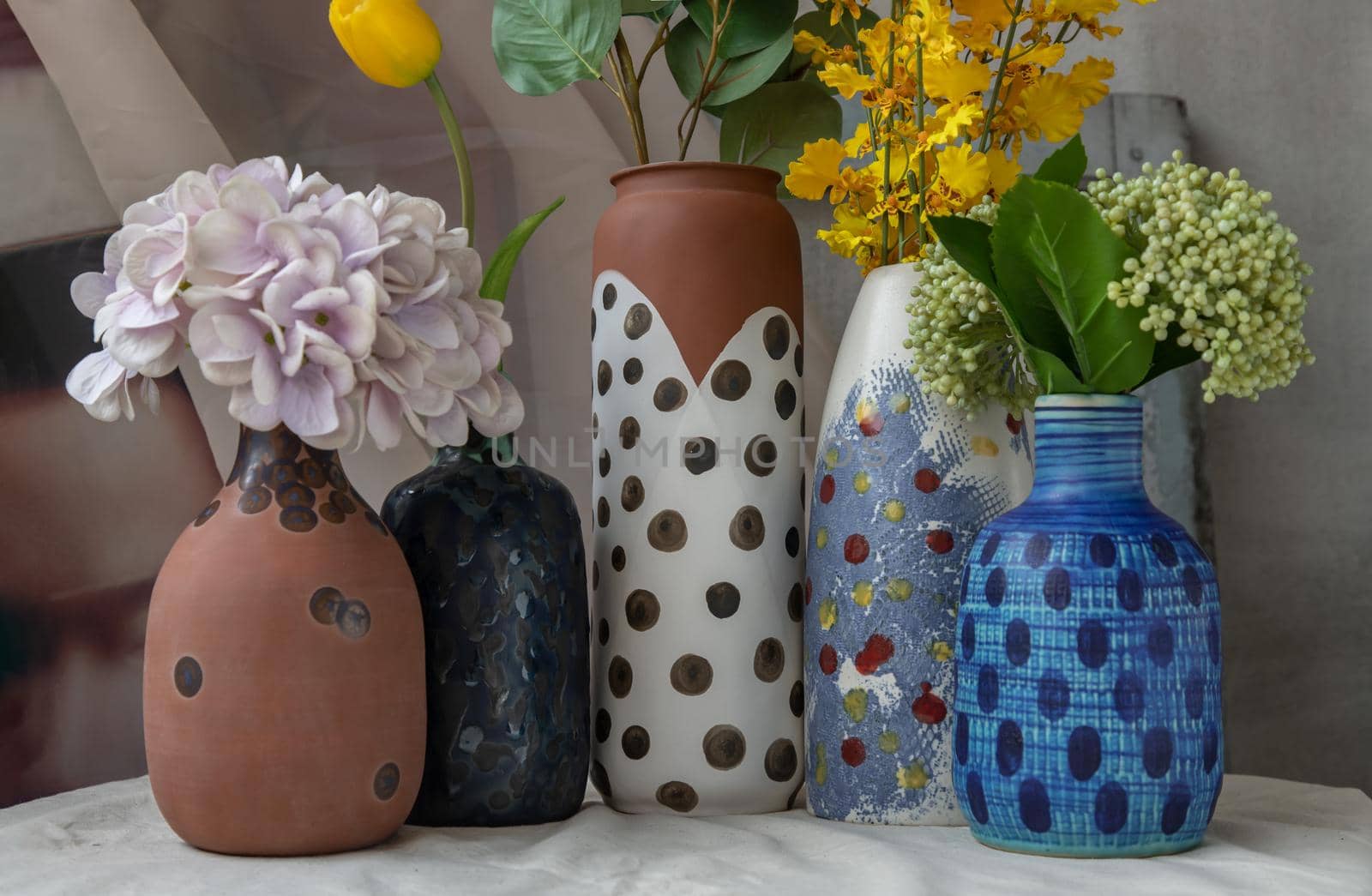 Bouquet of many flowers in Handmade Assorted Many Different Ceramic Polka Dotted Vases on white textured table cloth. Home decor, Space for text, Selective focus.
