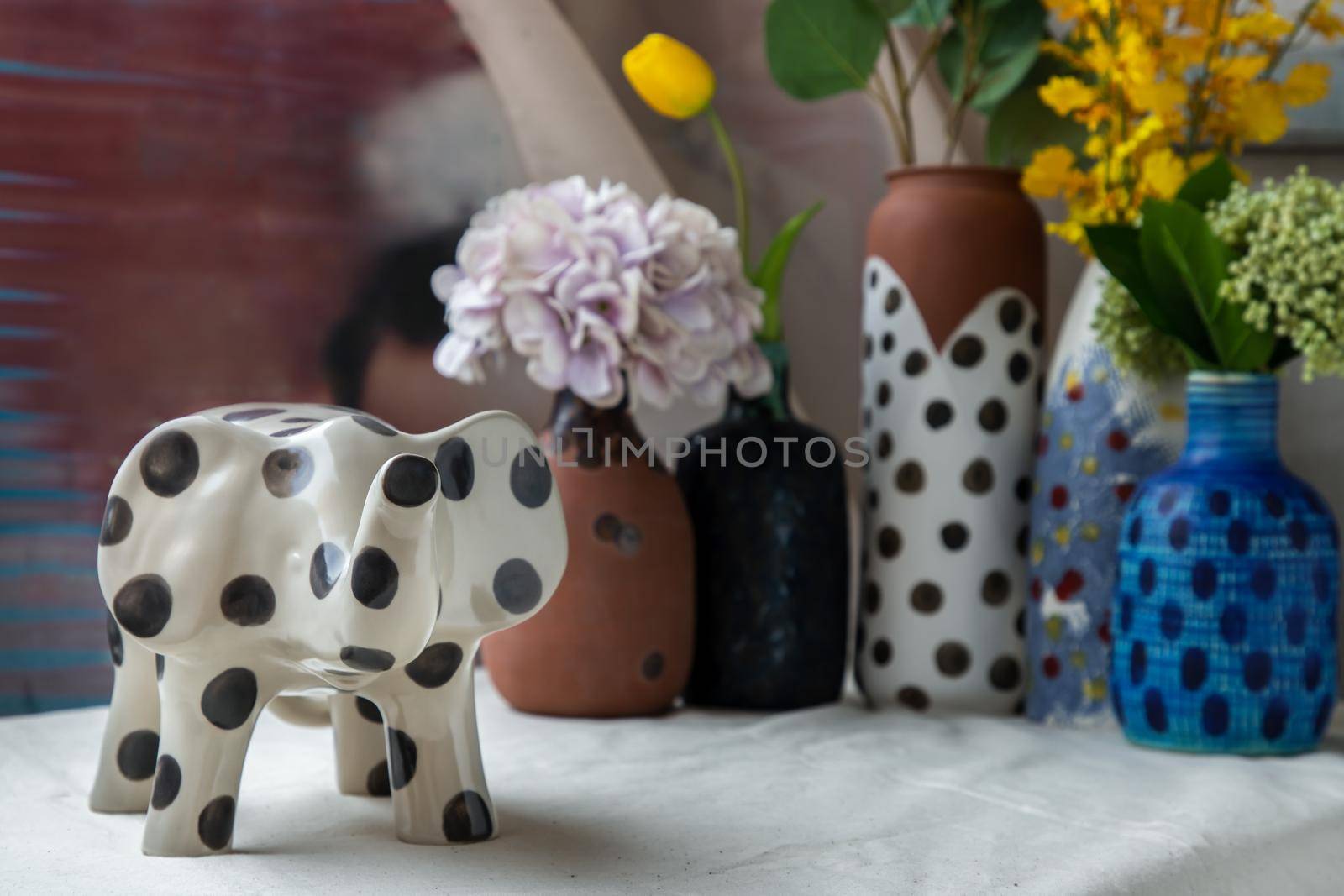 Bangkok, Thailand - Feb 06, 2021: Elephant shaped ceramic and Handmade Assorted Many Different Ceramic Polka Dotted Vases on white textured table cloth. Home decor, Space for text, Selective focus.