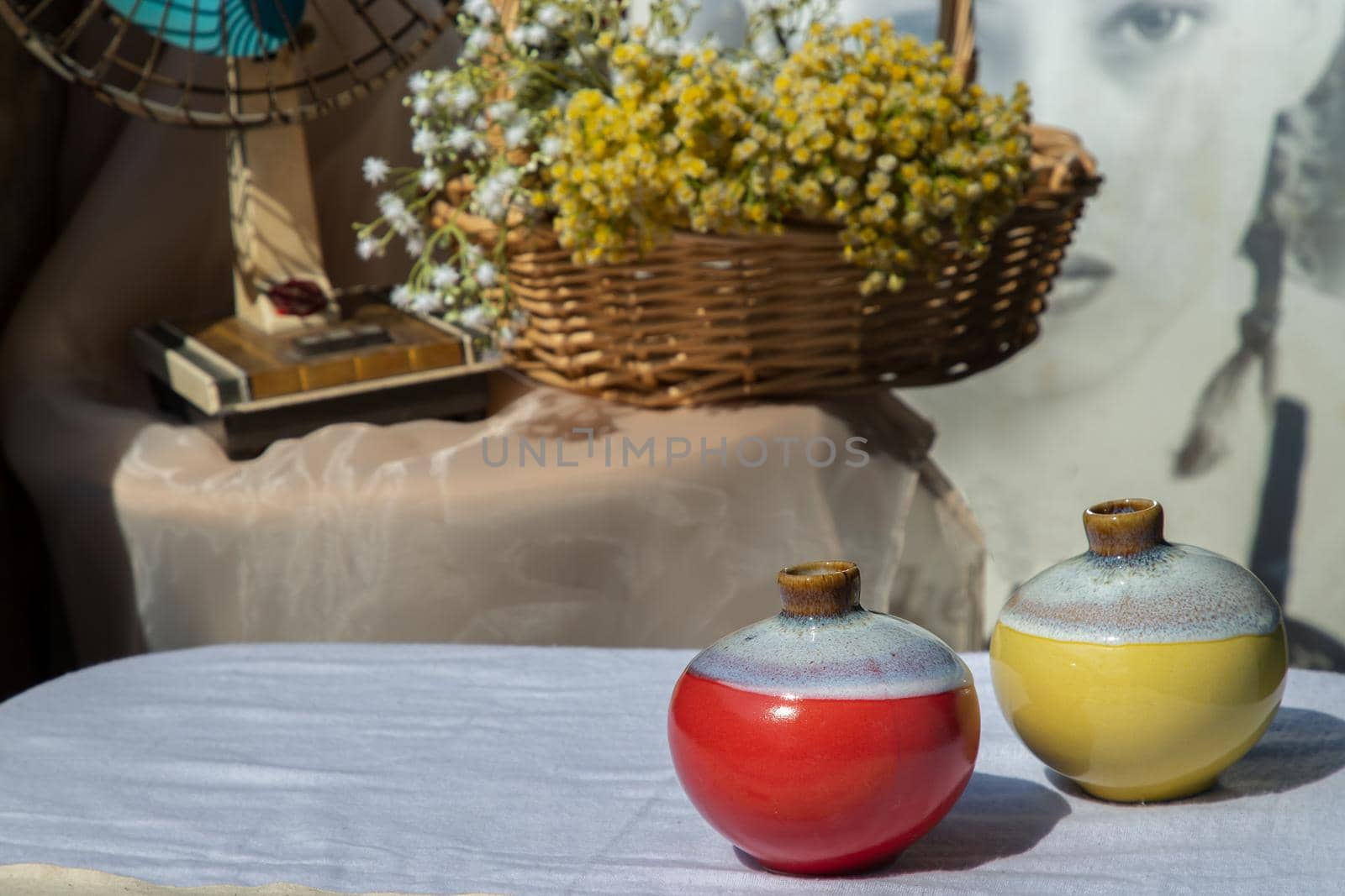Two small ceramic vases on white textured table cloth in front of Bouquet of flowers in woven basket and Vintage fan. Home decor, Selective focus.