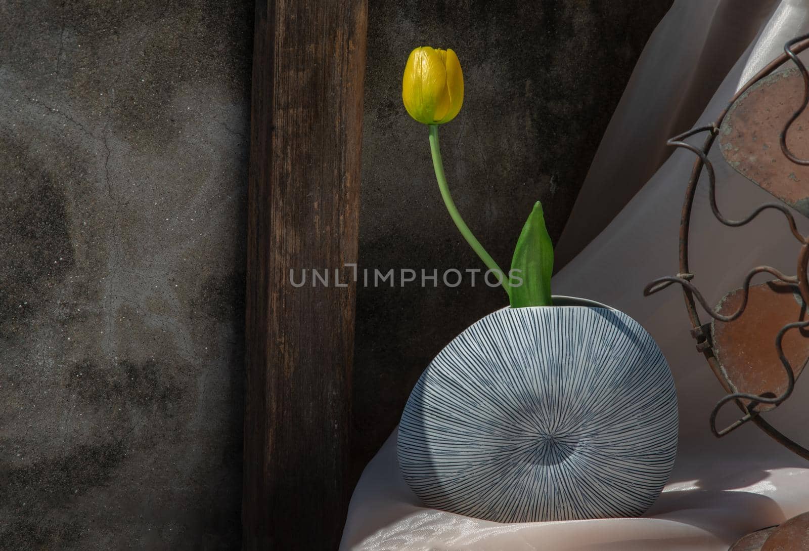 Yellow flower in Blue shell shape ceramic vase on pink textured table cloth with old cement wall.