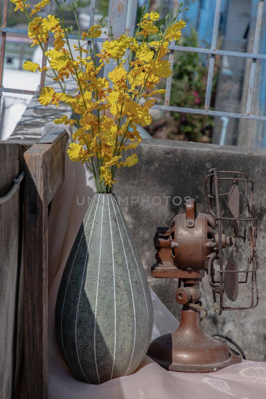 Bouquet of yellow flowers in Green watermel on shape ceramic vase and old vintage fan on pink textured table cloth with old cement wall at the balcony house. Home decor, Selective focus.