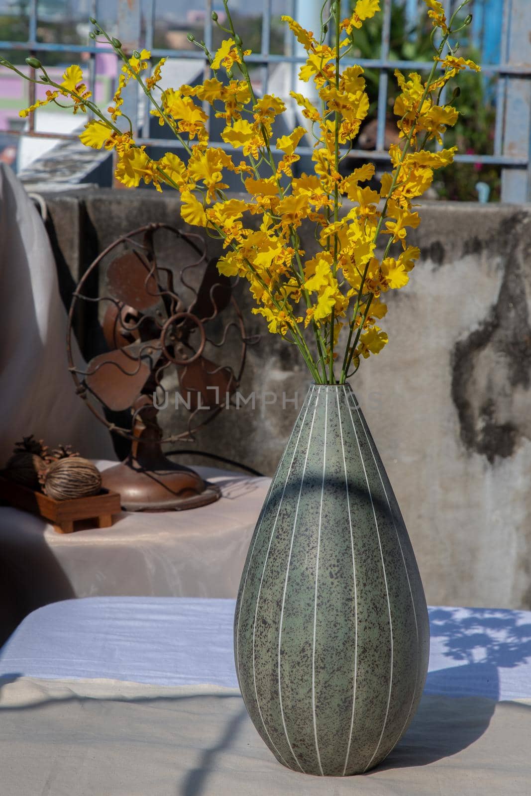 Bouquet of yellow flowers in Green watermel on shape ceramic vase and old vintage fan on pink textured table cloth with old cement wall at the balcony house. Home decor, Selective focus.