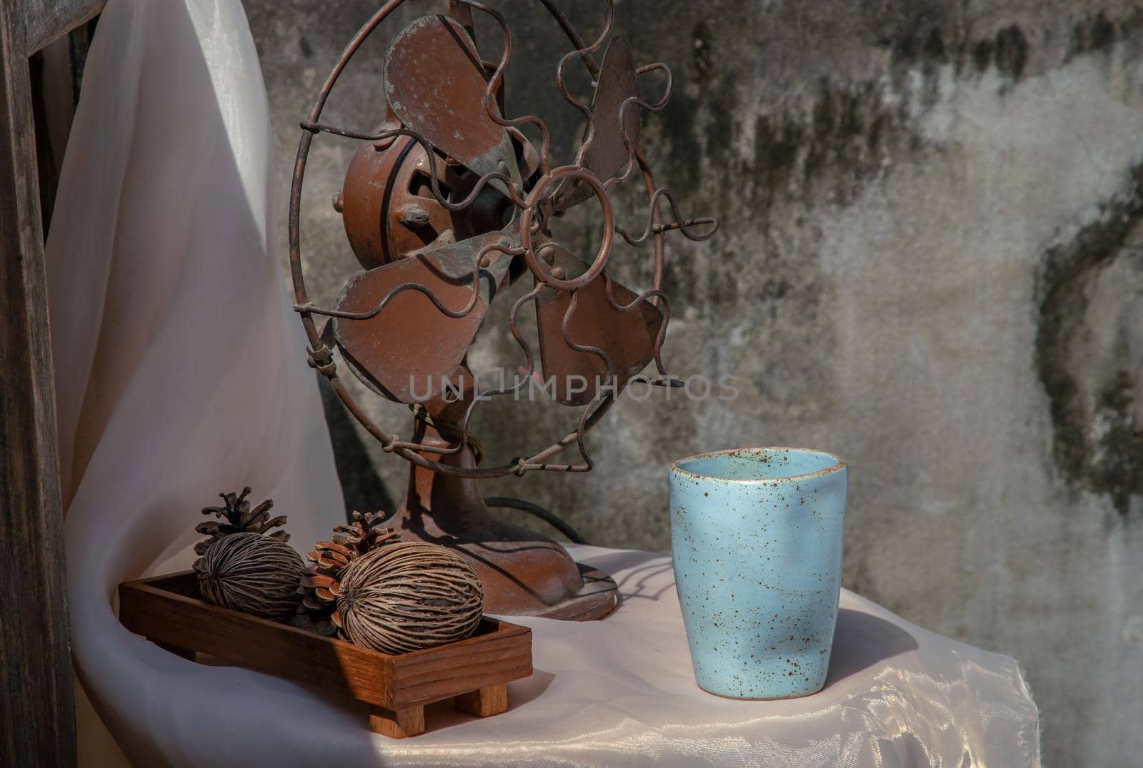 Old vintage brown metal fan and Dried cerbera oddloam's with Blue ceramic mug handmade on pink table with old ruins cement wall. Selective focus.