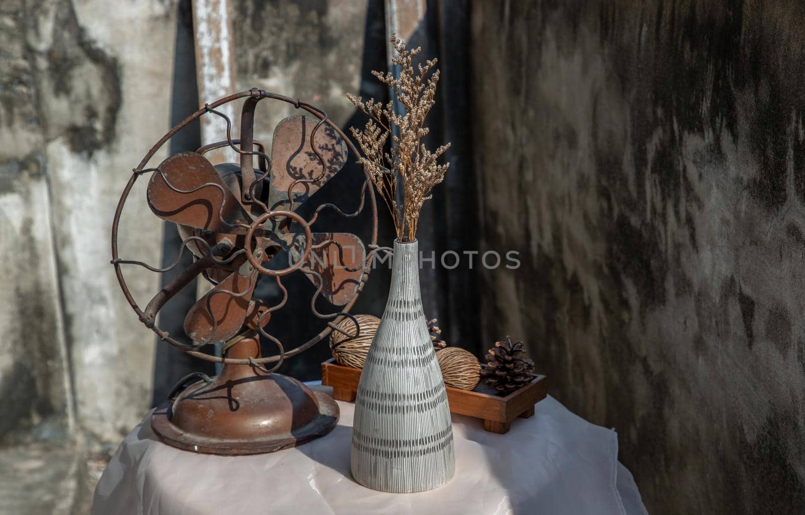 Dried flowers in Ceramic vase on pink textured table cloth and vintage fan with Old cement wall. Home decor, Selective focus.