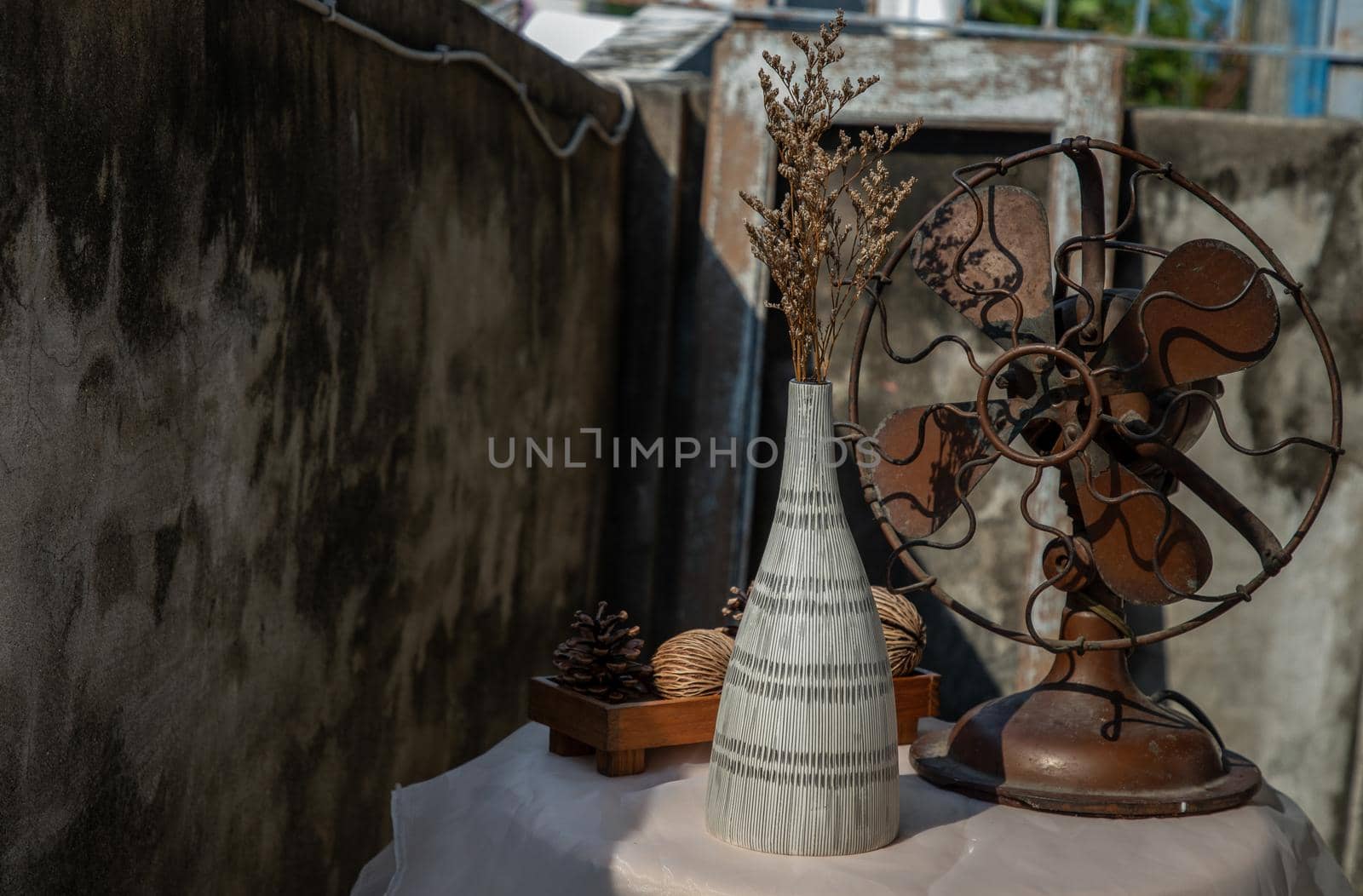 Dried flowers in Ceramic vase on pink textured table cloth and vintage fan with Old cement wall. Home decor, Selective focus.