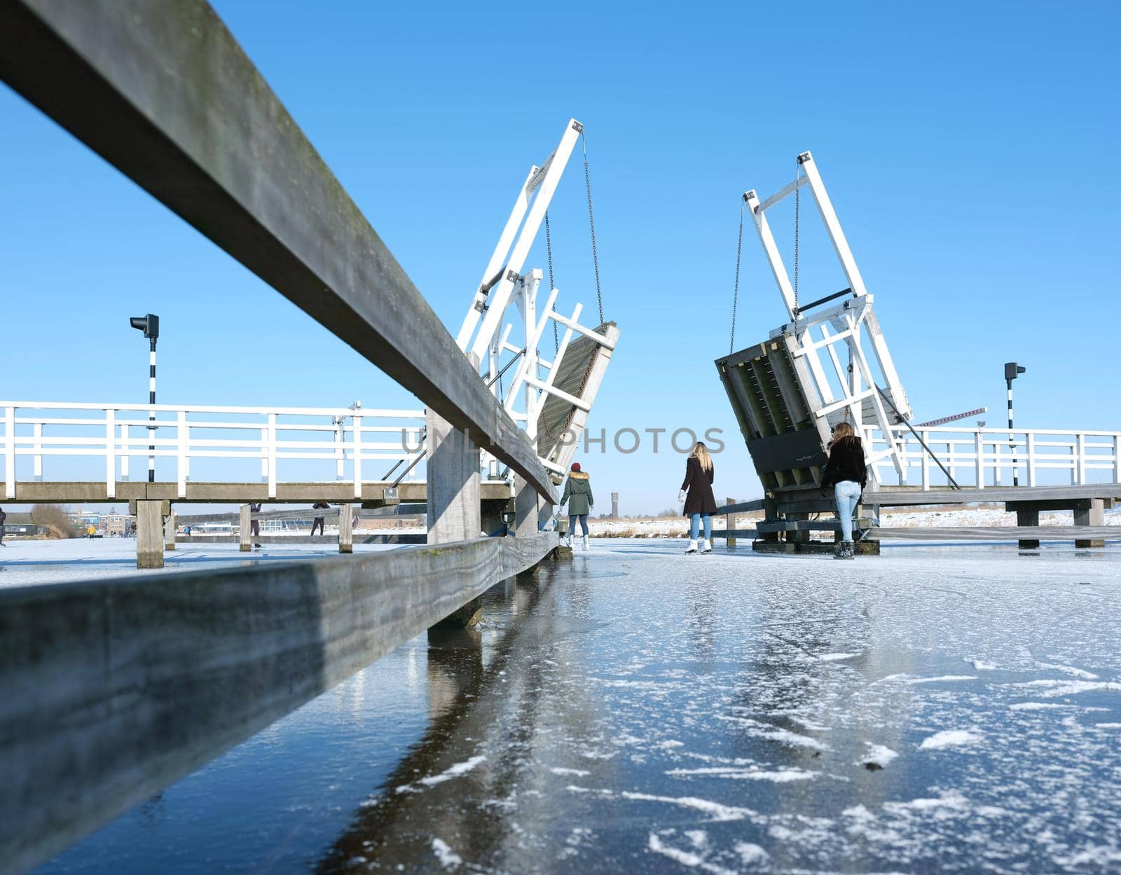 people skate through drawbridge in kinderdijk on frozen water of canal on sunny winter day in the netherlands
