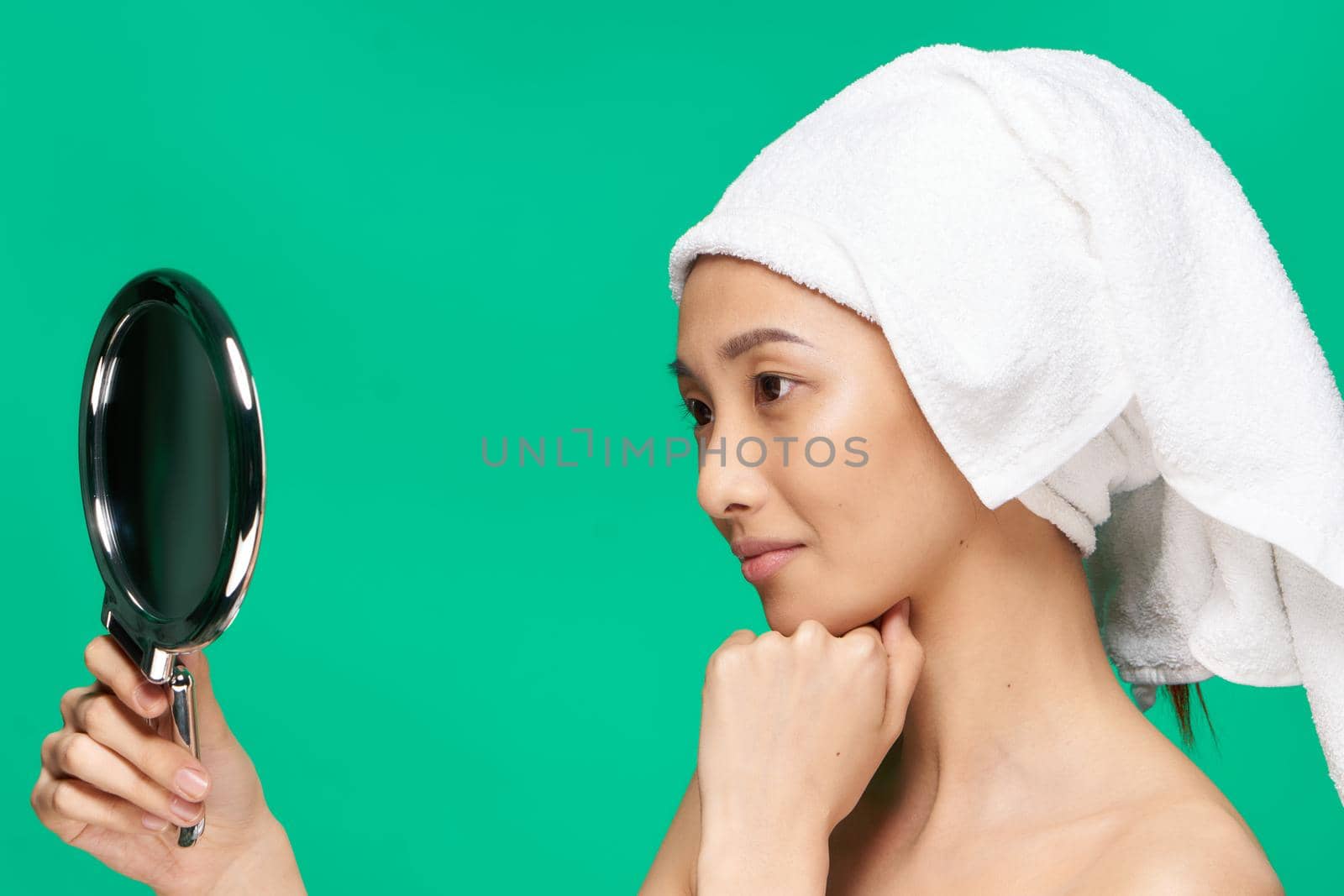 woman of Asian appearance with a towel on her head naked shoulders Looking in the mirror. High quality photo