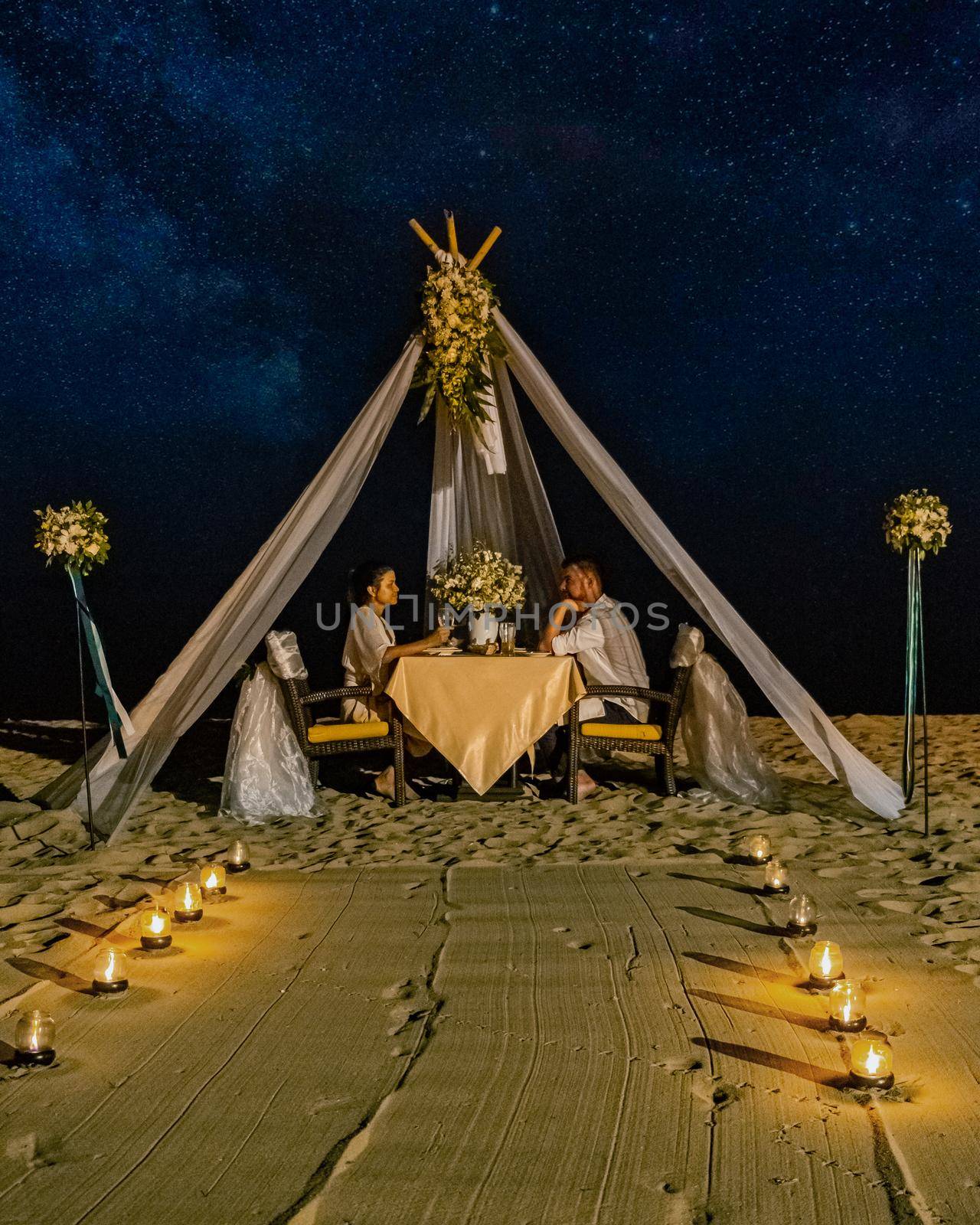 couple men and woman having romantic dinner with candle lights on the beach in Thailand, European men and Asian woman dinner on the beach Valentine concept by fokkebok