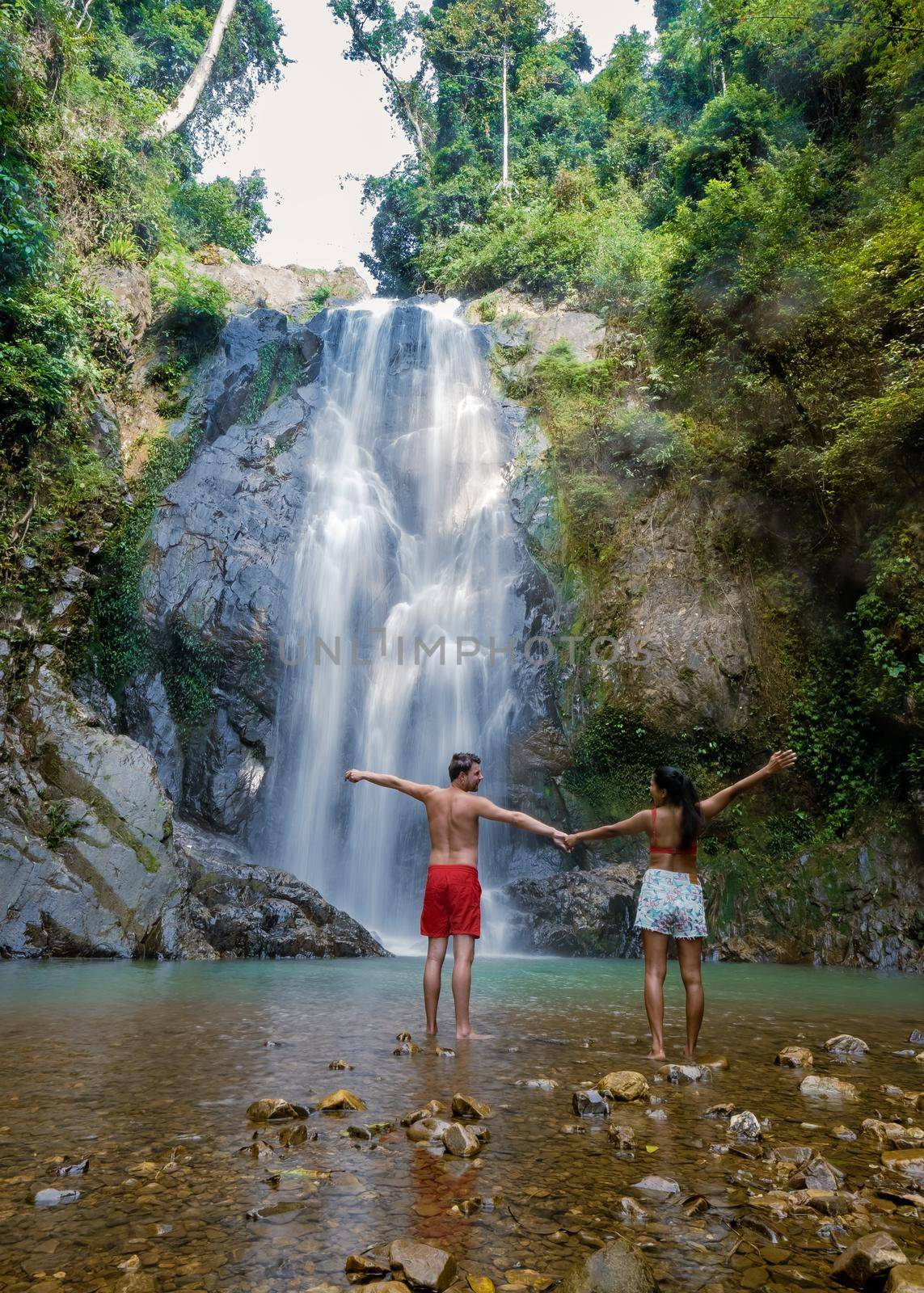 couple men and woman mid age visiting a waterfall in Thailand, A tourist is enjoying the beauty of the waterfall in Chumphon province, Thailand , Klongphrao waterfall Thailand by fokkebok