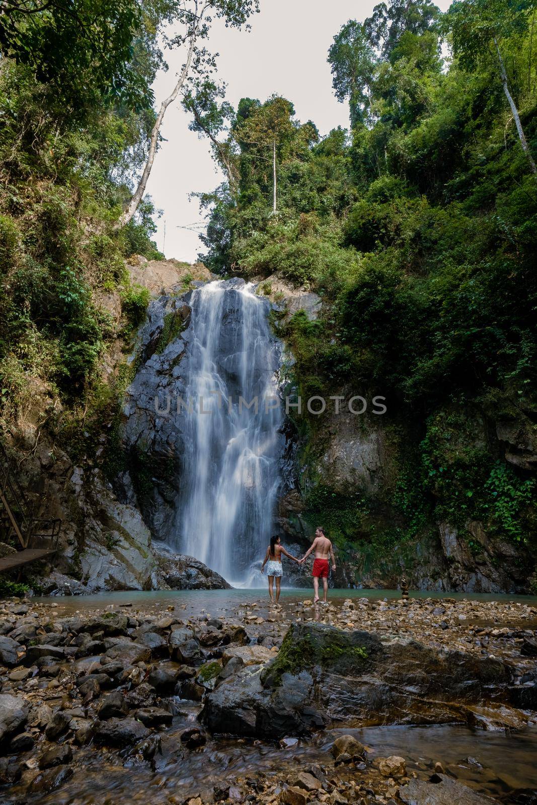 couple men and woman mid age visiting a waterfall in Thailand, A tourist is enjoying the beauty of the waterfall in Chumphon province, Thailand , Klongphrao waterfall Thailand by fokkebok