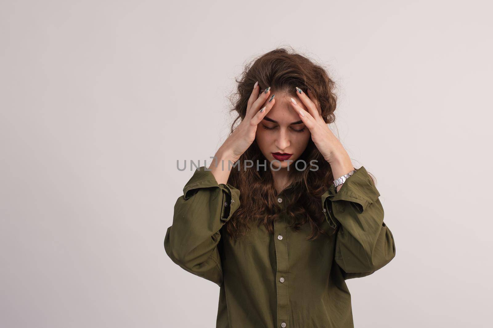 A beautiful girl has a migraine and a headache. A young woman holds her hands to her temples and massages them. On a gray background. copy space