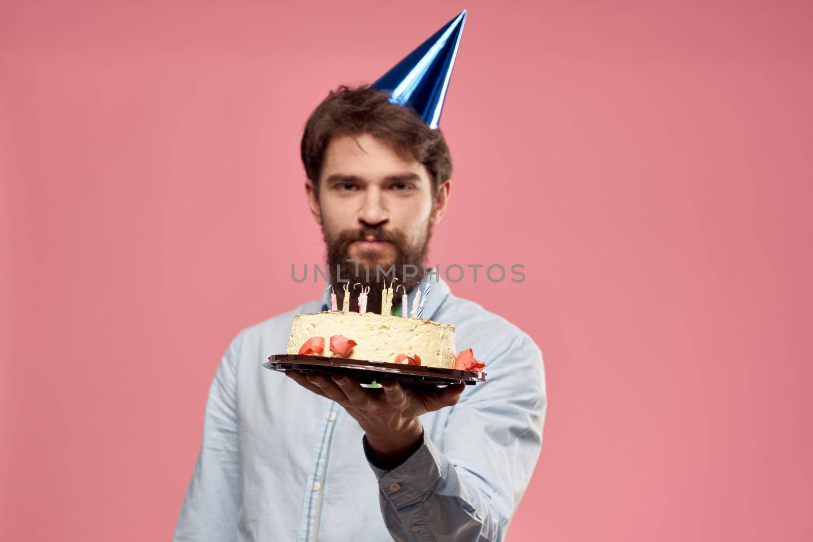 Man with cake in a plate and in a blue shirt on a pink background birthday holidays cropped view. High quality photo