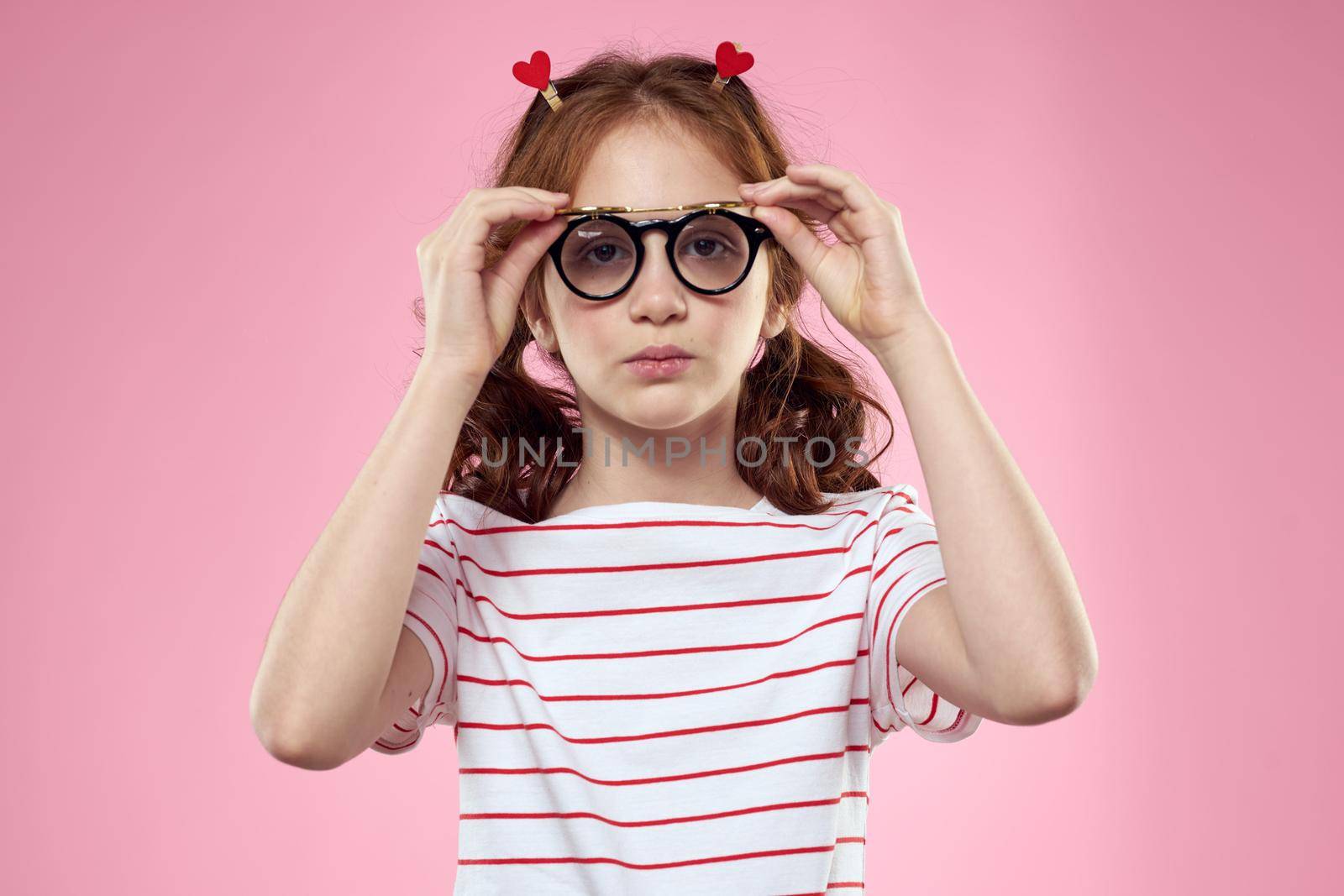 little girl in fashionable glasses and clothespins on her hair emotions pink background hearts. High quality photo