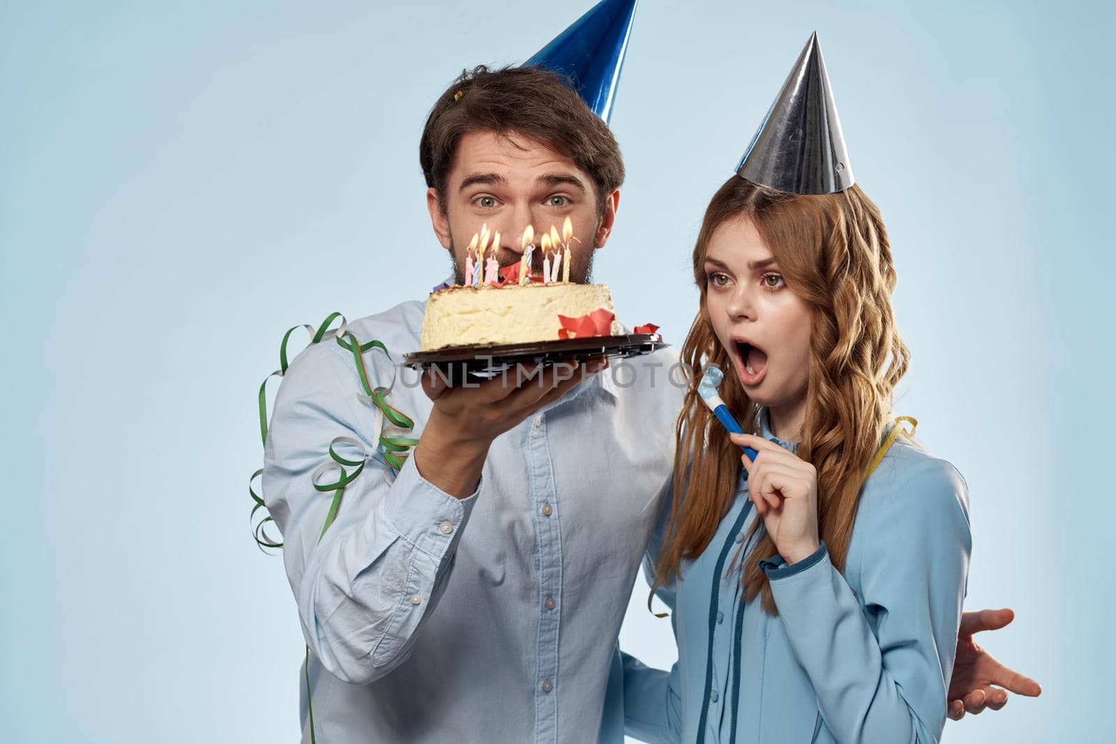 man and woman celebrate birthday with cake and in hats on blue background. High quality photo