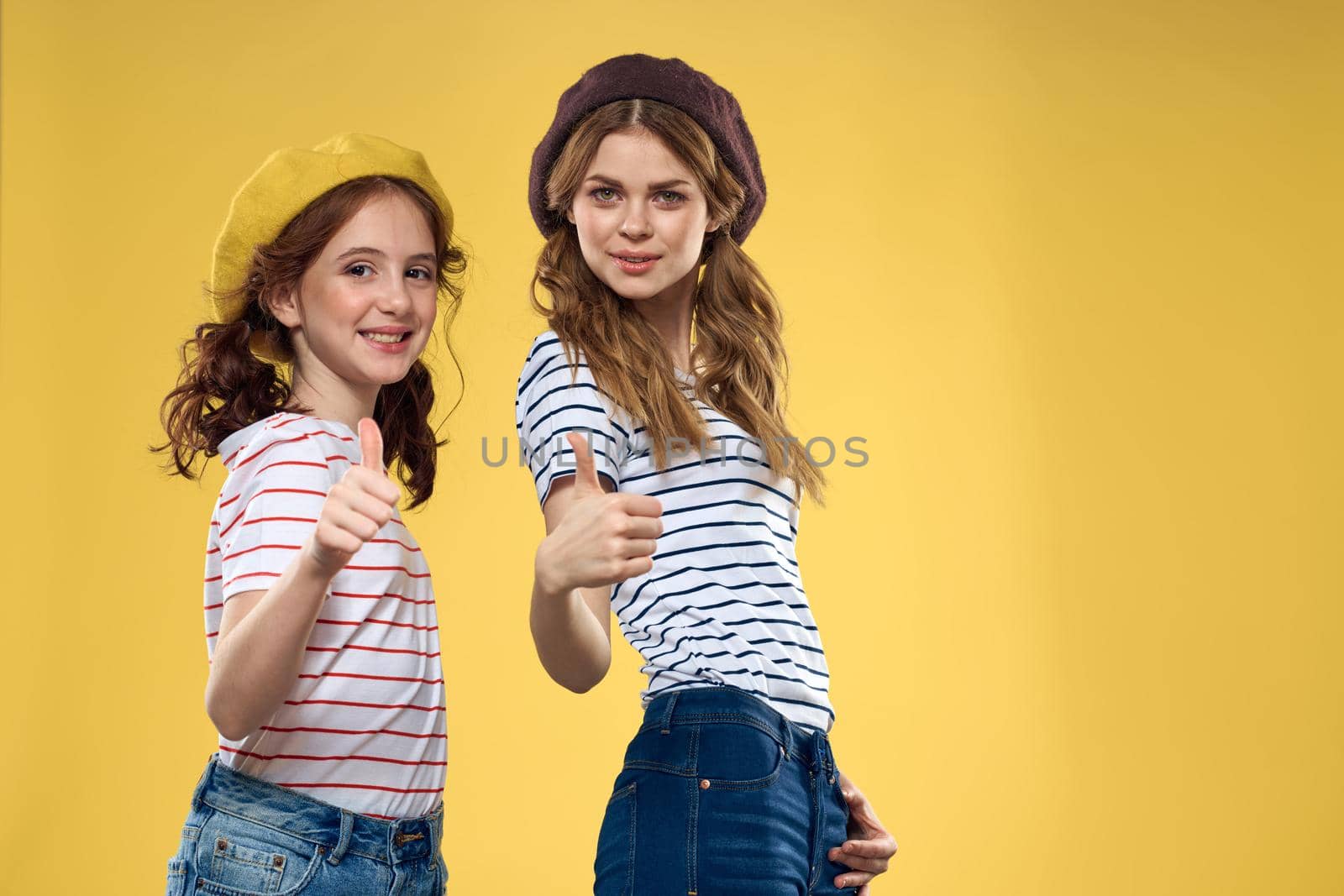 Cheerful sisters in hats striped T-shirts joy lifestyle yellow background family. High quality photo