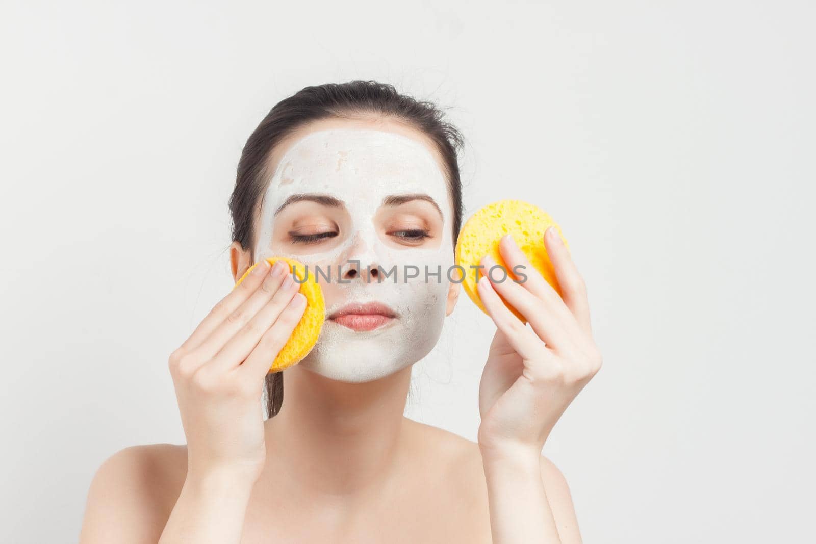 joyful woman with bare shoulders cream mask on face scrub sponges in hands. High quality photo