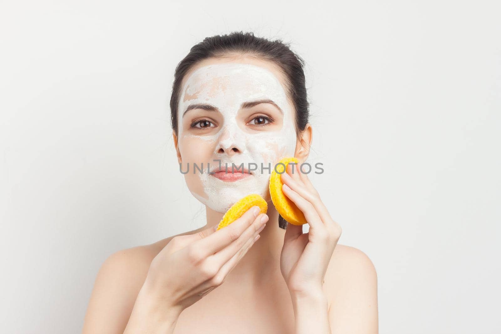 joyful woman with bare shoulders cream mask on face scrub sponges in hands. High quality photo