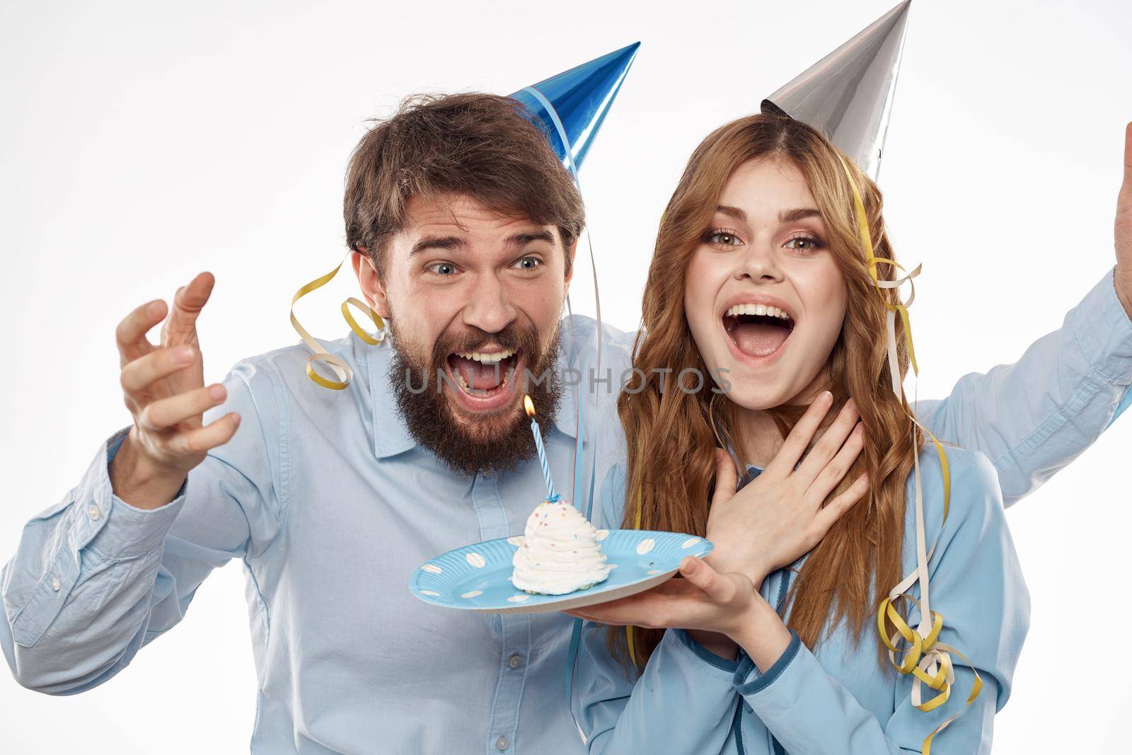 energetic man and woman with a cake and in hats celebrate a birthday on a light background. High quality photo