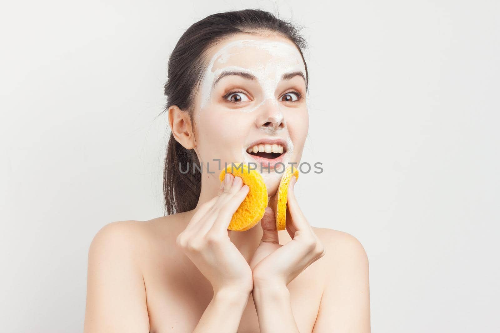 cheerful brunette with bare shoulders face mask sponges in hands skin care. High quality photo