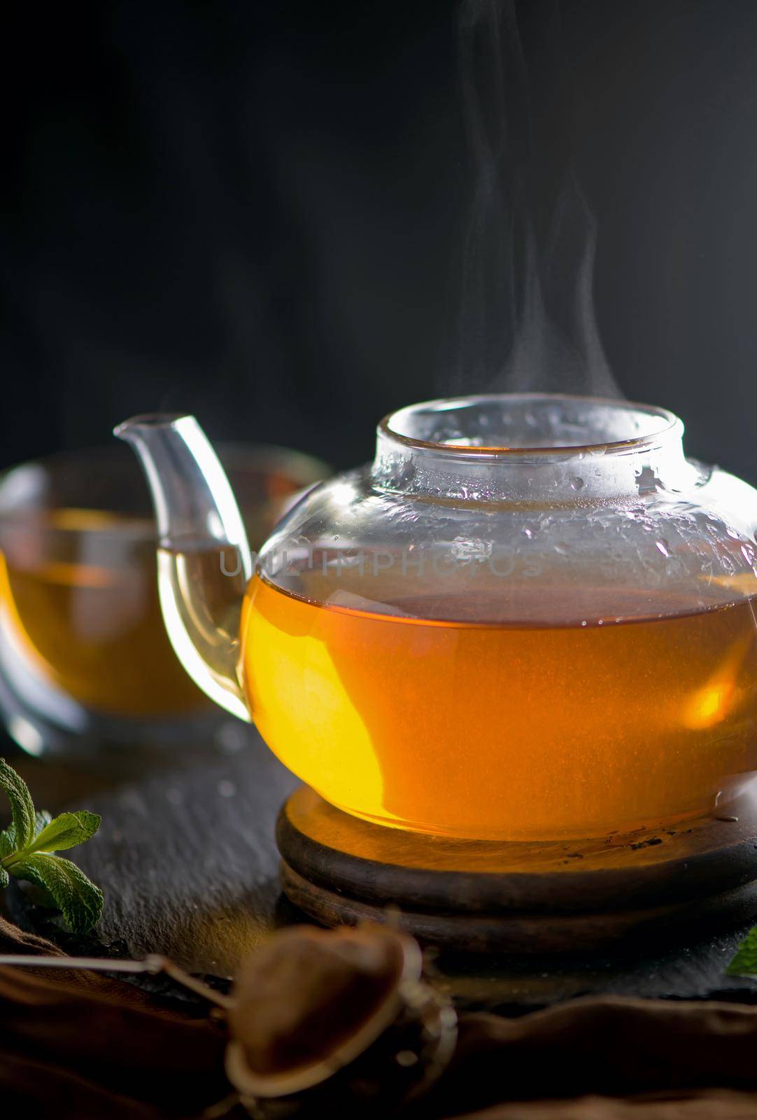 Teapot with tea surrounded with green leaves, tea ceremony, green tea in a transparent cup