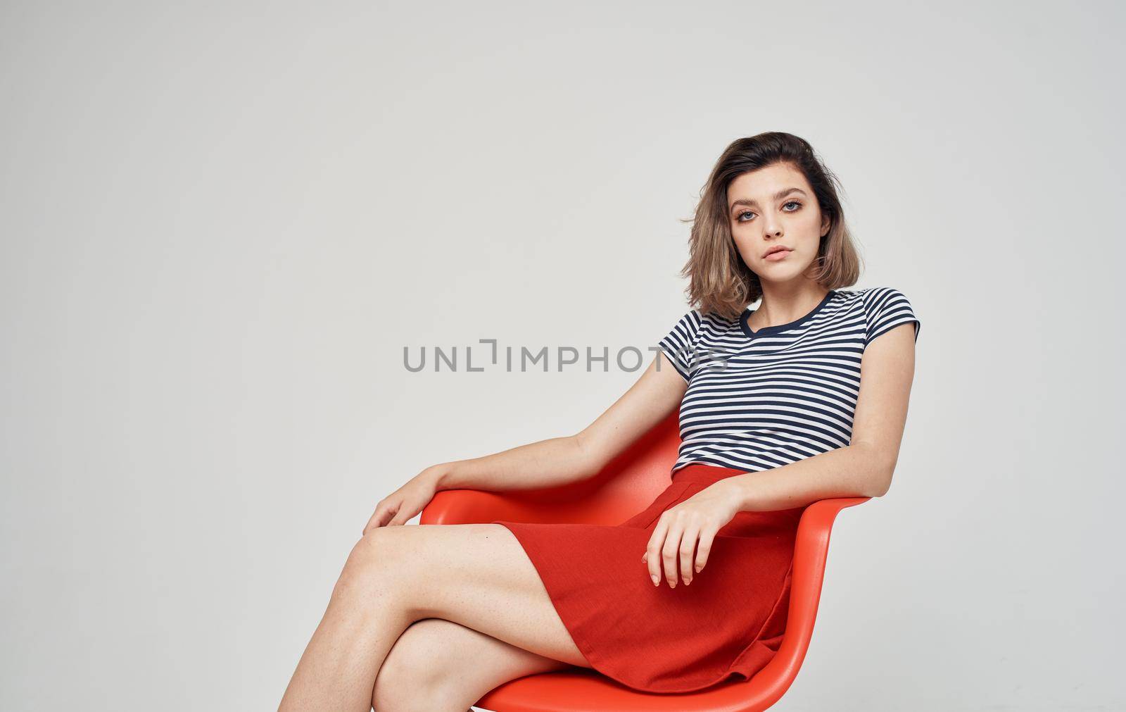fashionable woman in a striped t-shirt sits on a red chair In a bright room Copy Space. High quality photo