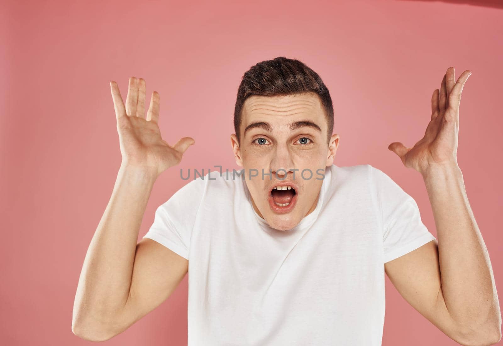 man in white t-shirt emotions gestures with hands pink background. High quality photo