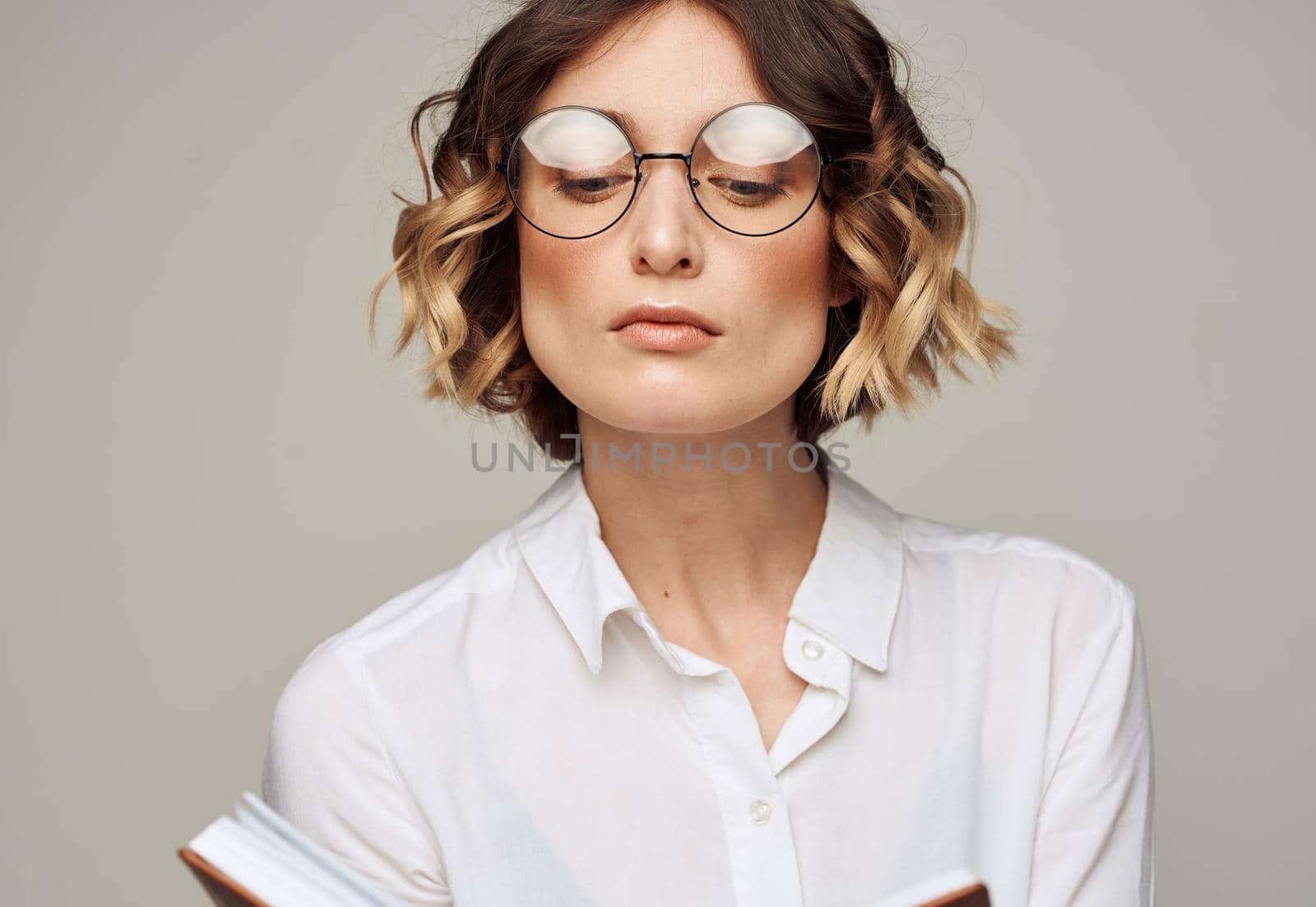Woman with a notepad in her hands and wearing glasses on a gray background cropped view of a Light shirt. High quality photo