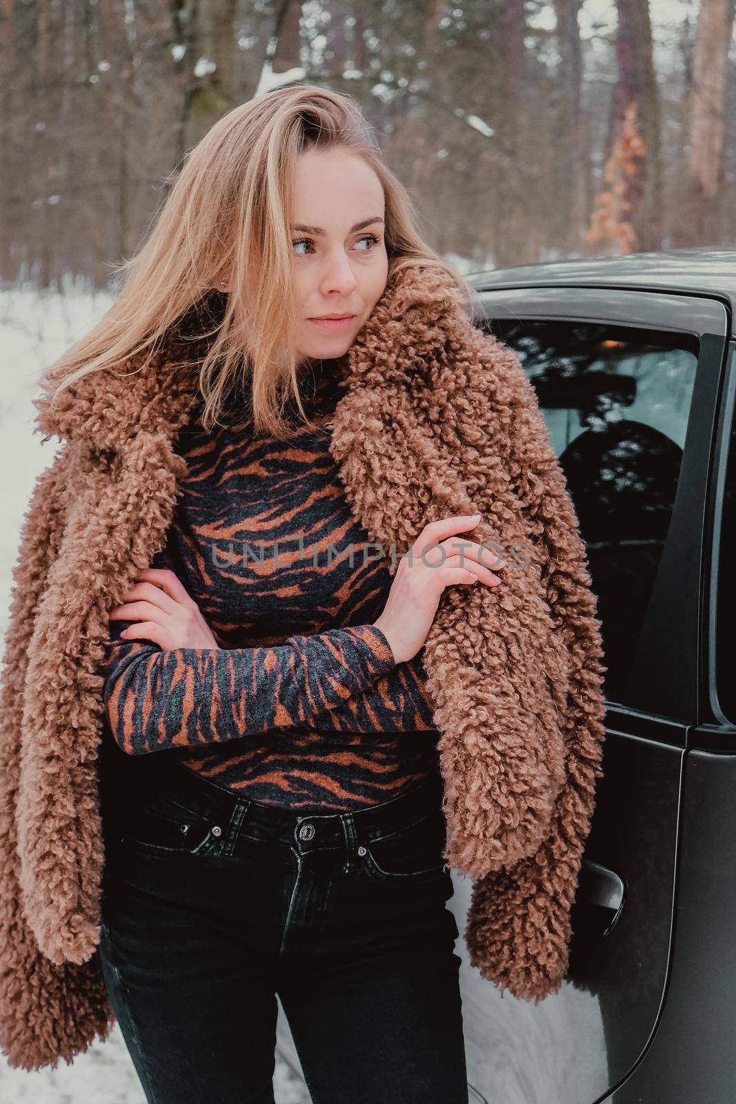 Attractive beautiful young woman in sweater staying next to the car in forest. Winter vacation. Holidays. Smilling Christmas lights.