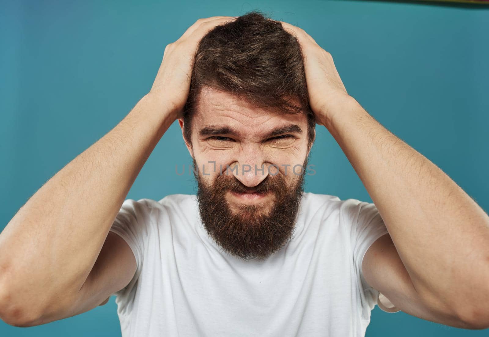 Upset man with a beard touches his head with his hands on a blue background by SHOTPRIME