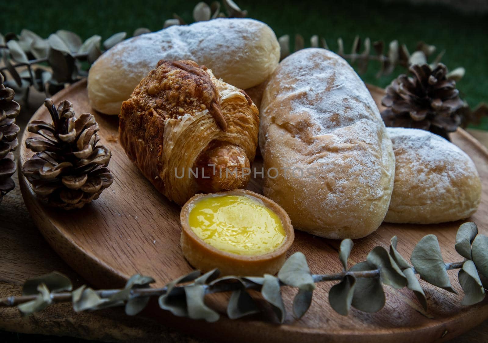 Homemade sweet cream soft buns, Baked croissant sausage and Lemon tart with Dried flowers on round wooden plate over rustic wooden table. Bakery and dessert concept, Selective focus.