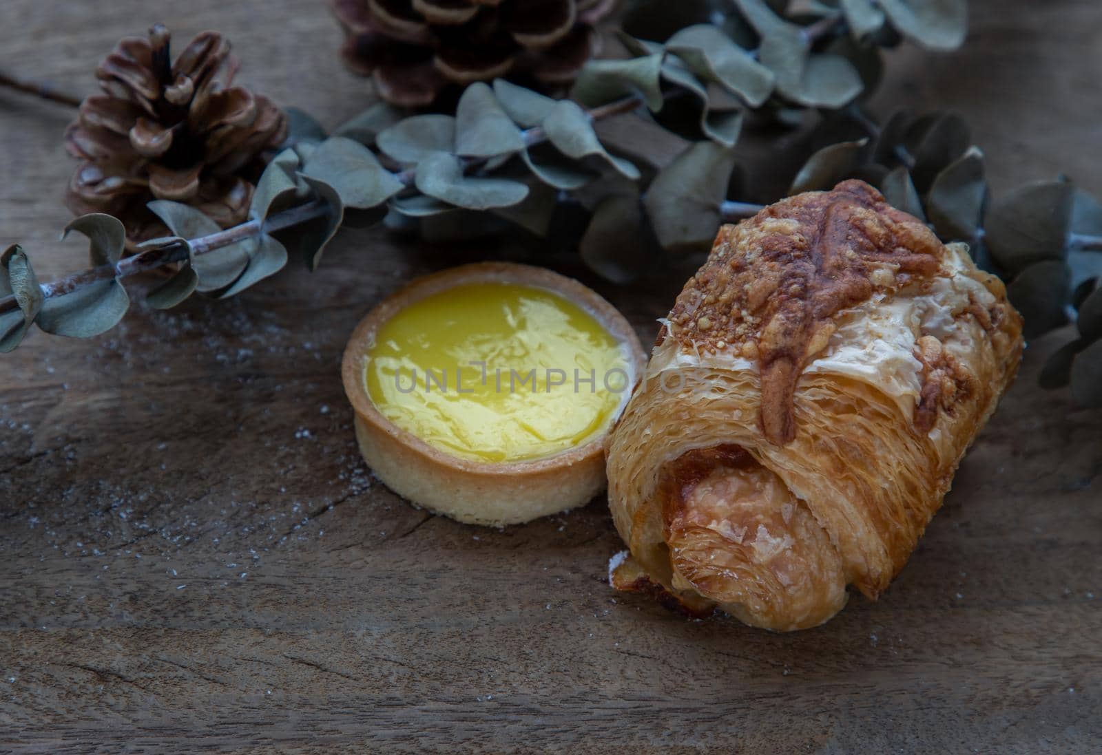 Baked croissant sausage and Lemon tart with Dried flowers on old rustic wooden table. Bakery and dessert concept, Selective focus.