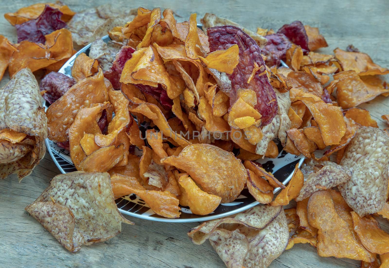 Mixed thai sweets made from sliced sweet potato coated with sugar (Potato chip) on ceramic plate over rustic wooden background. Selective focus.