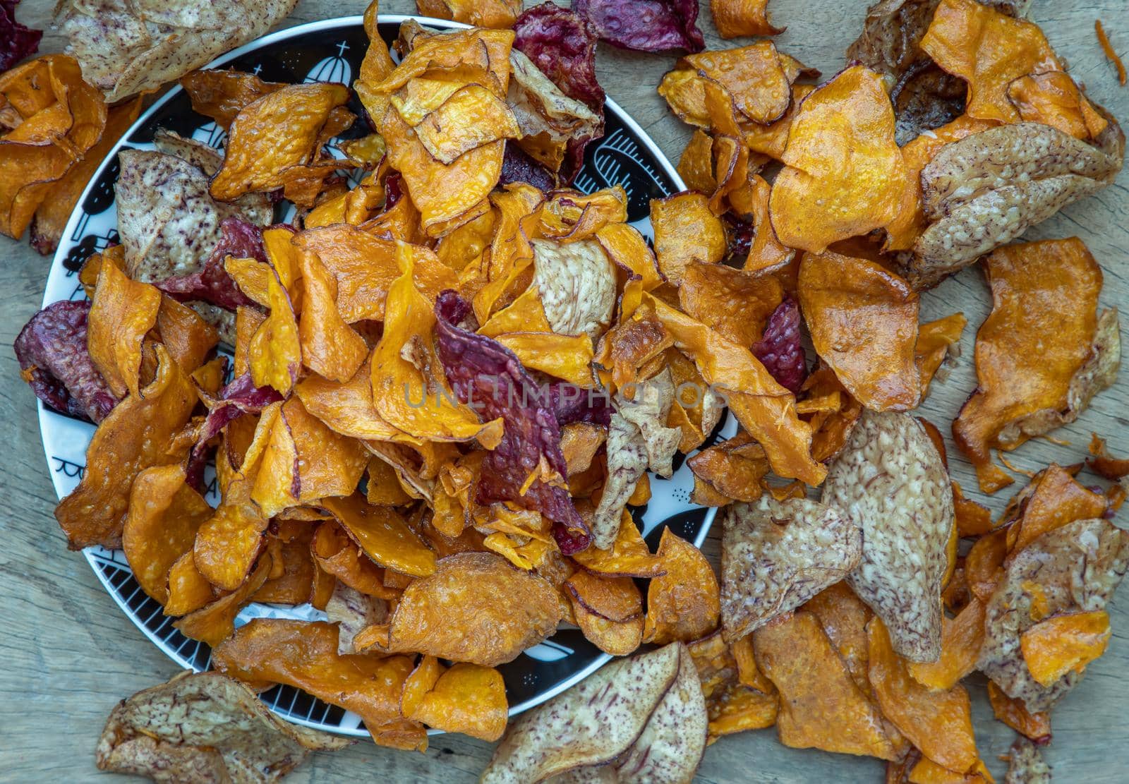 Mixed thai sweets made from sliced sweet potato coated with sugar (Potato chip) on ceramic plate over rustic wooden background. Selective focus.