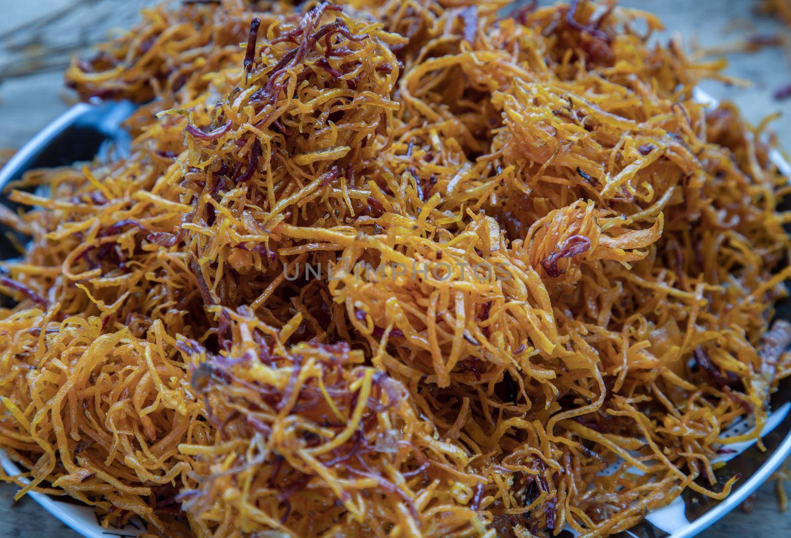 Thai sweets made from shredded sweet potato coated with sugar (Thai sweetmeat made of fried sweet potato) on ceramic plate over rustic wooden background. Selective focus