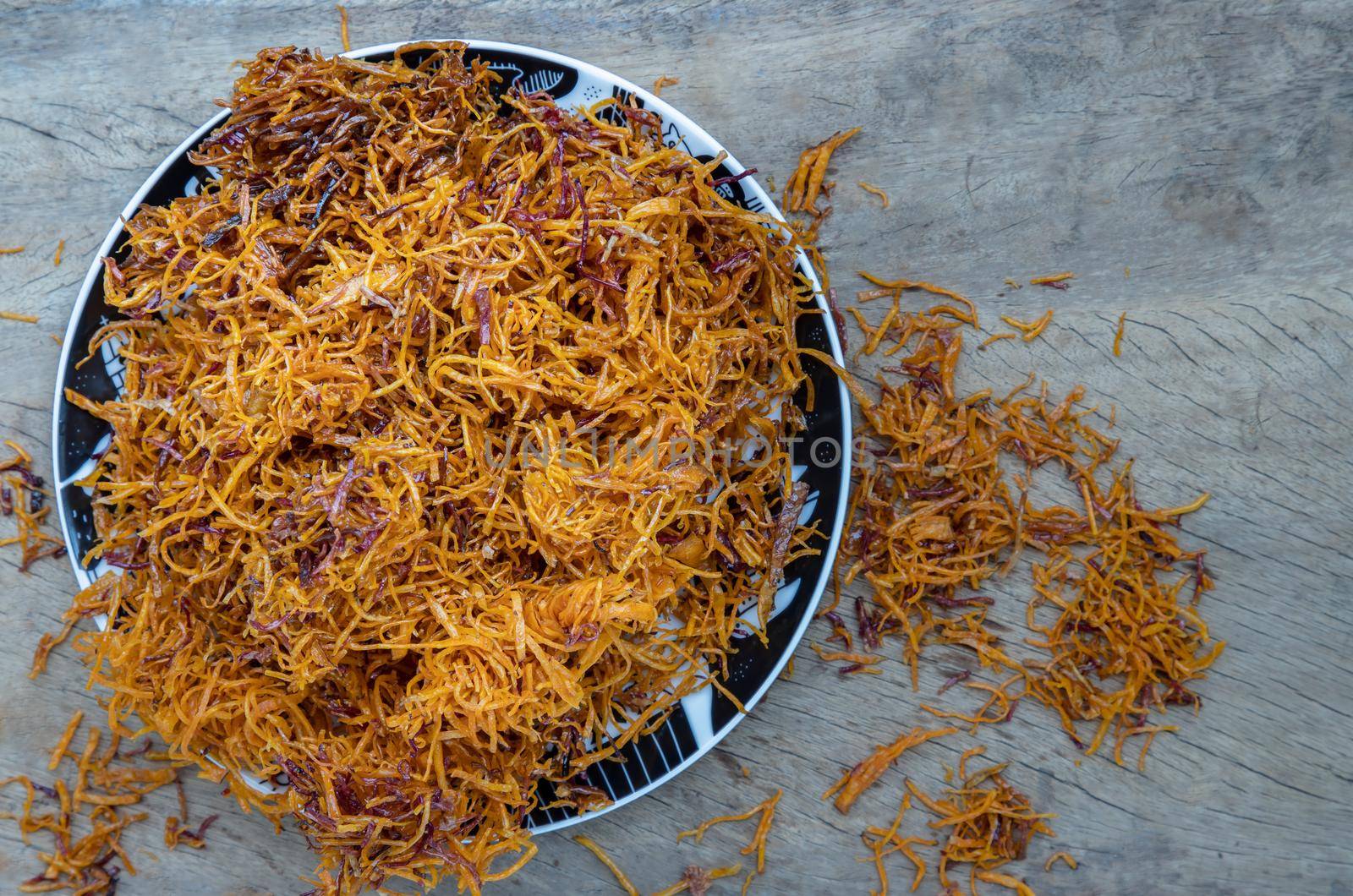 Thai sweets made from shredded sweet potato coated with sugar (Thai sweetmeat made of fried sweet potato) on ceramic plate over rustic wooden background. Selective focus.
