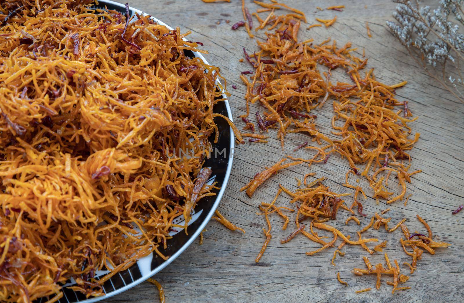 Thai sweets made from shredded sweet potato coated with sugar (Thai sweetmeat made of fried sweet potato) on ceramic plate over rustic wooden background. Selective focus.