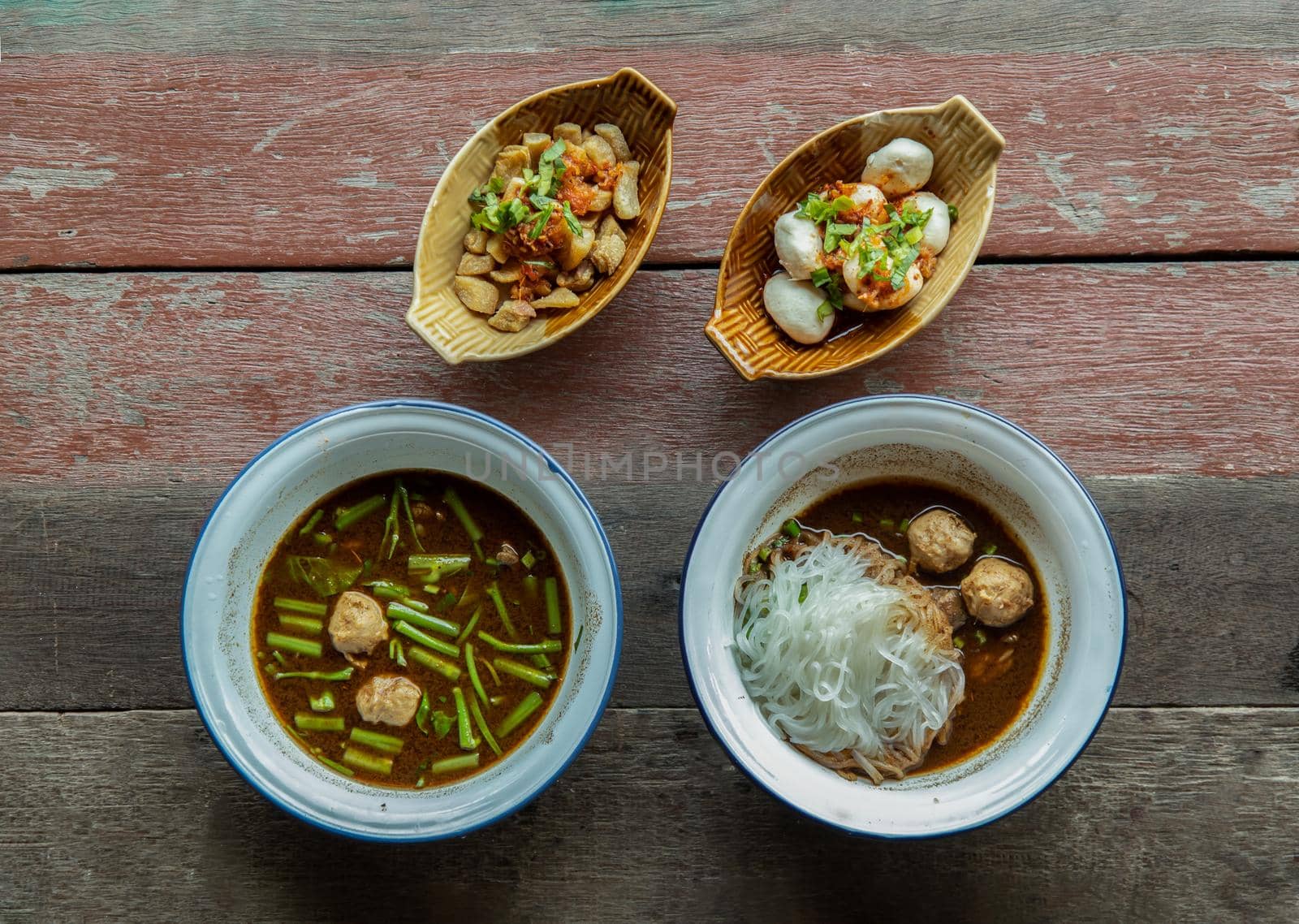 Thai style boat noodles "Kuay Tiew Rua" in Tile bowl with Pork crackling and pork balls on rustic wooden table. Selective focus.