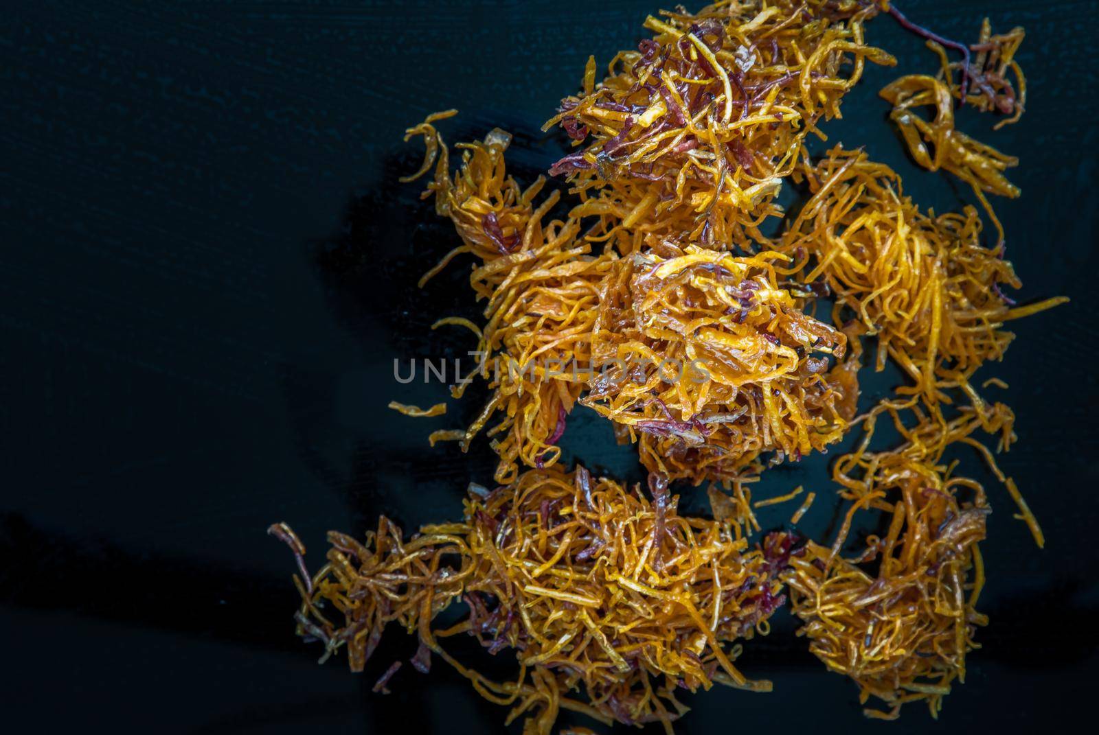 Thai sweets made from shredded sweet potato coated with sugar (Thai sweetmeat made of fried sweet potato) on black table.  Copy spce, Selective focus.