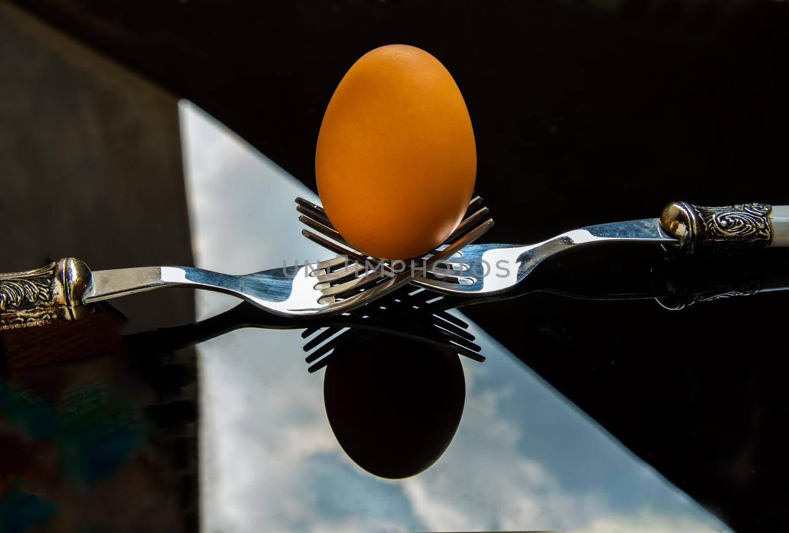 Fresh chicken egg (Hen egg) balanced on a composition of two intertwined forks over black table. Selective focus.