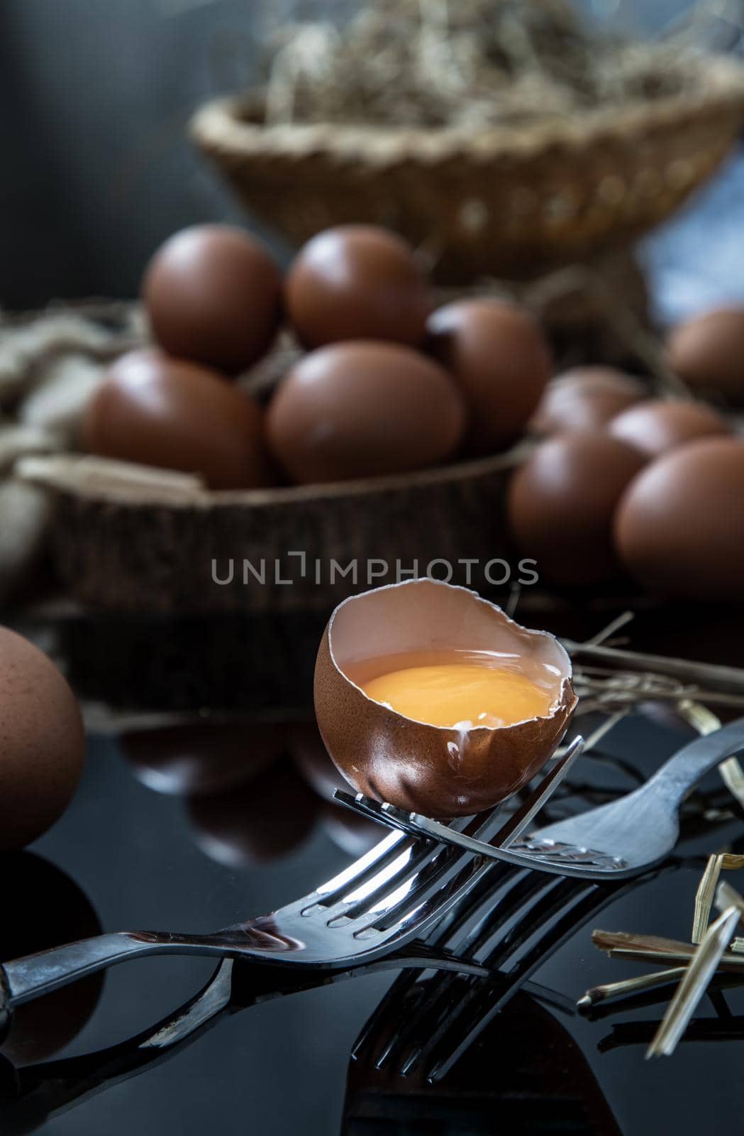 Broken fresh chicken egg (Hen egg) balanced on a composition of two intertwined forks with fresh chicken eggs on wood background. Selective focus.