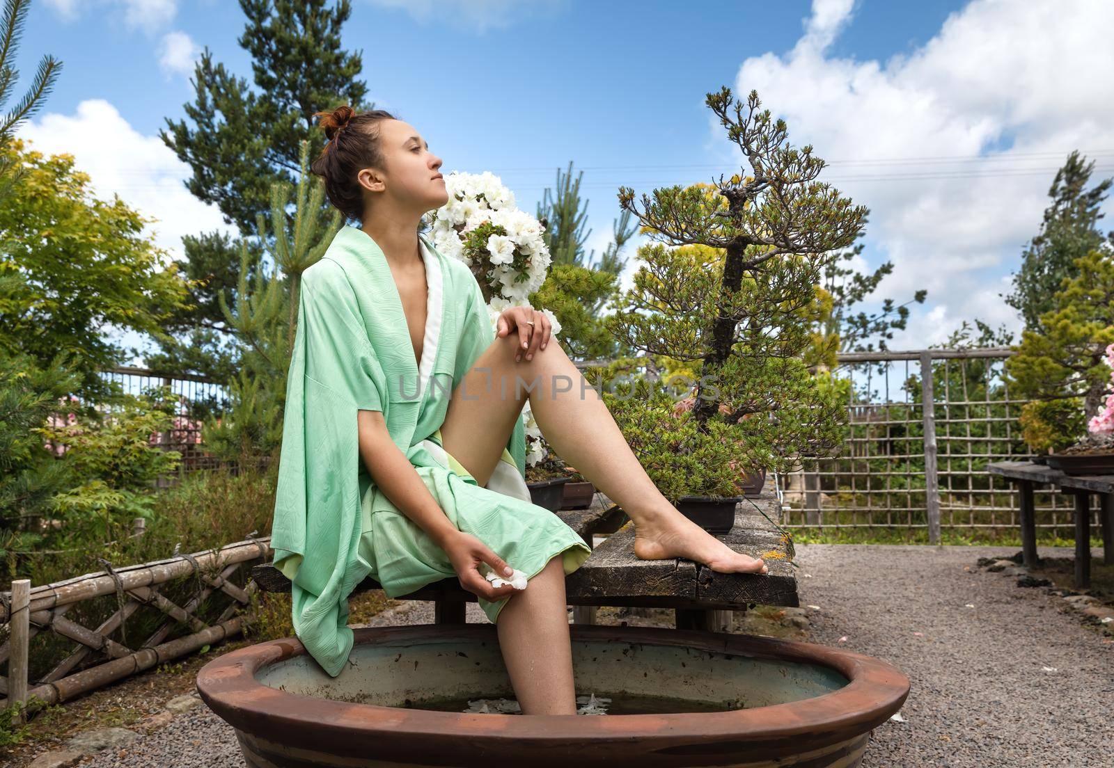 Japanese Garden. Young beautiful woman dressed in Japanese kimono at the garden enjoying the beauty of nature and blooming flowers