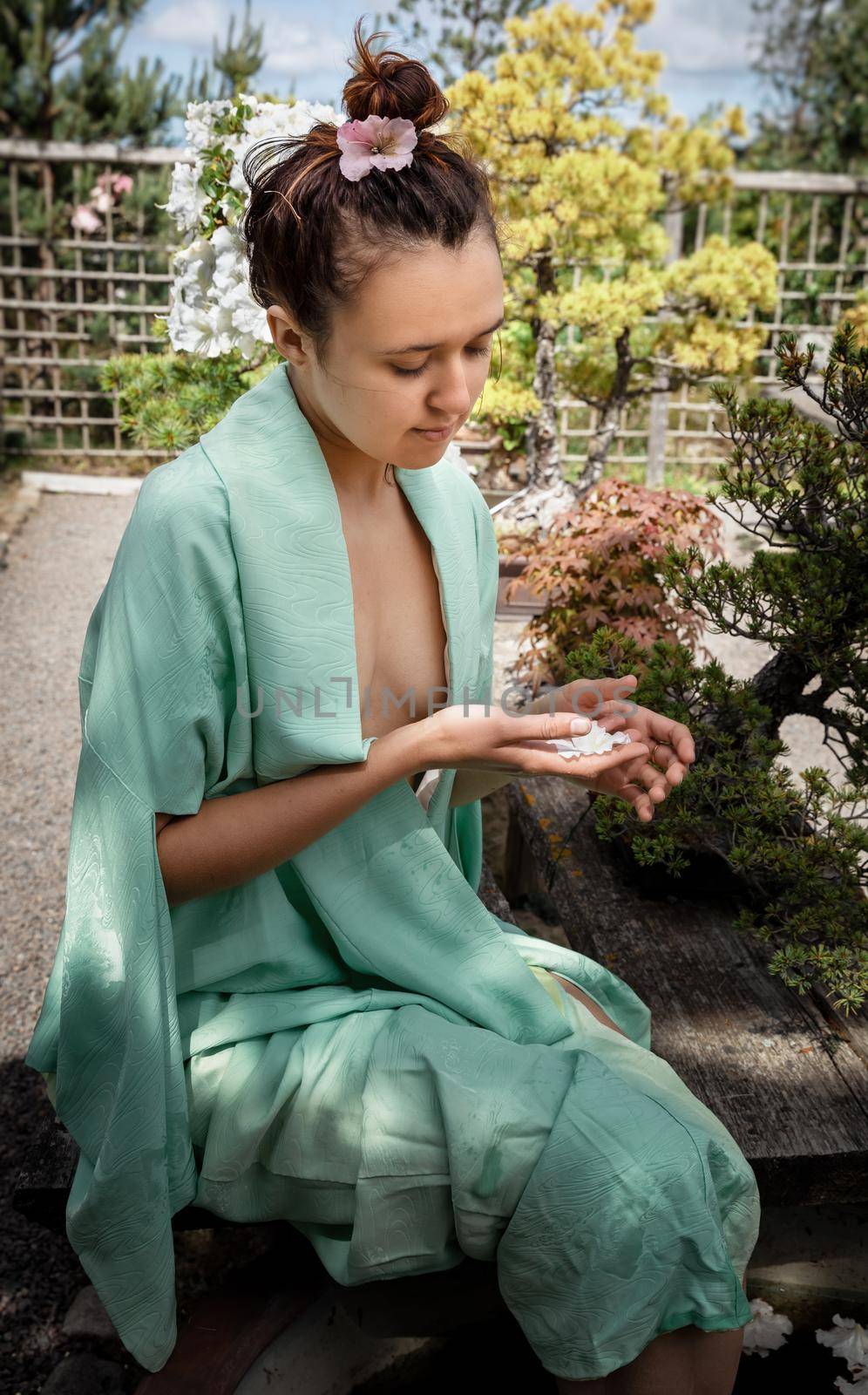 Japanese Garden. Young beautiful woman dressed in Japanese kimono at the garden enjoying the beauty of nature and blooming flowers