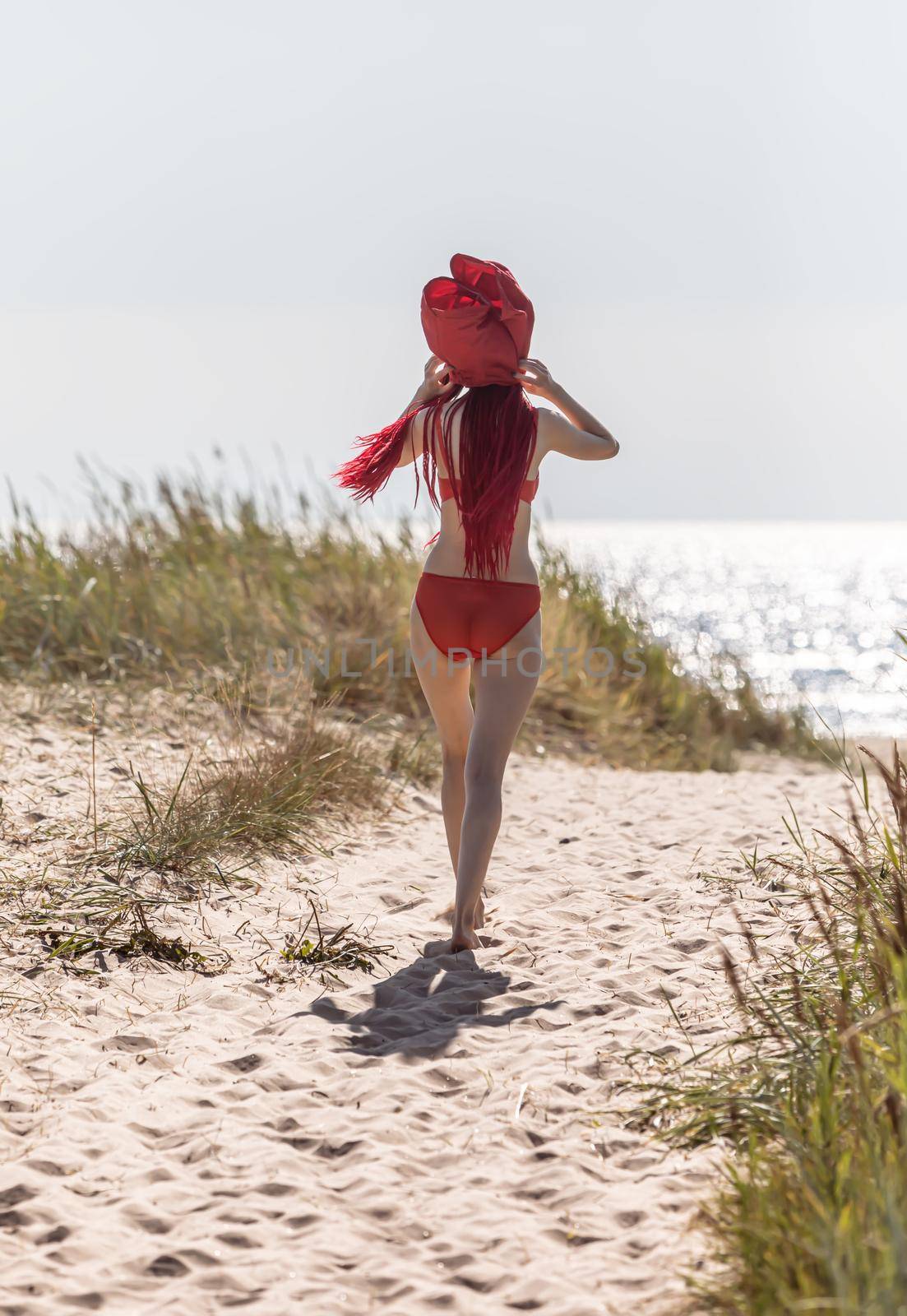 Beautiful young woman with scarlet dreadlocks and red bathing suit enjoying nature. 