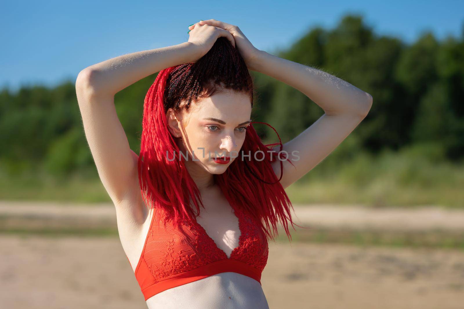 Beautiful young woman with scarlet dreadlocks and red bathing suit enjoying nature. 
